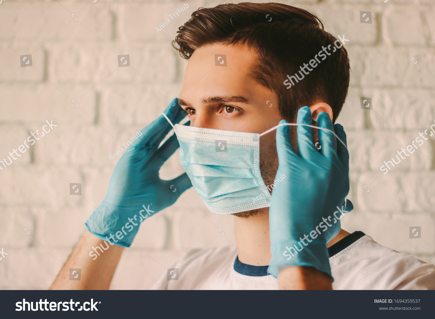 Confident young surgeon doctor in latex protective gloves wearing medical mask on face. Man professional medic in medical gloves put on protective face mask. Personal protection. Coronavirus COVID-19 #1694359537