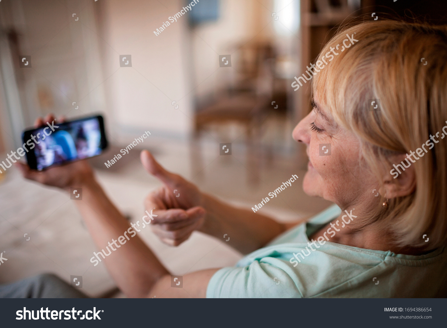 A senior woman talking with her grandchild within video chat via smartphone, digital conversation, life in quarantine time, self-isolation #1694386654