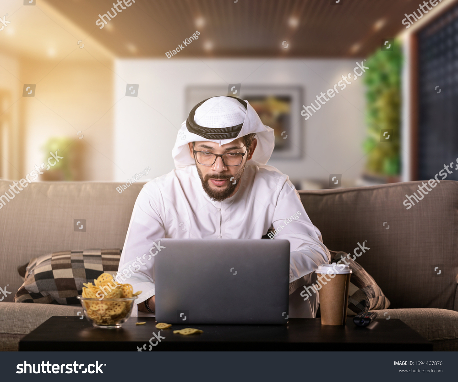 Arab man working from home sitting on sofa night time. coronavirus Quarantine. #1694467876