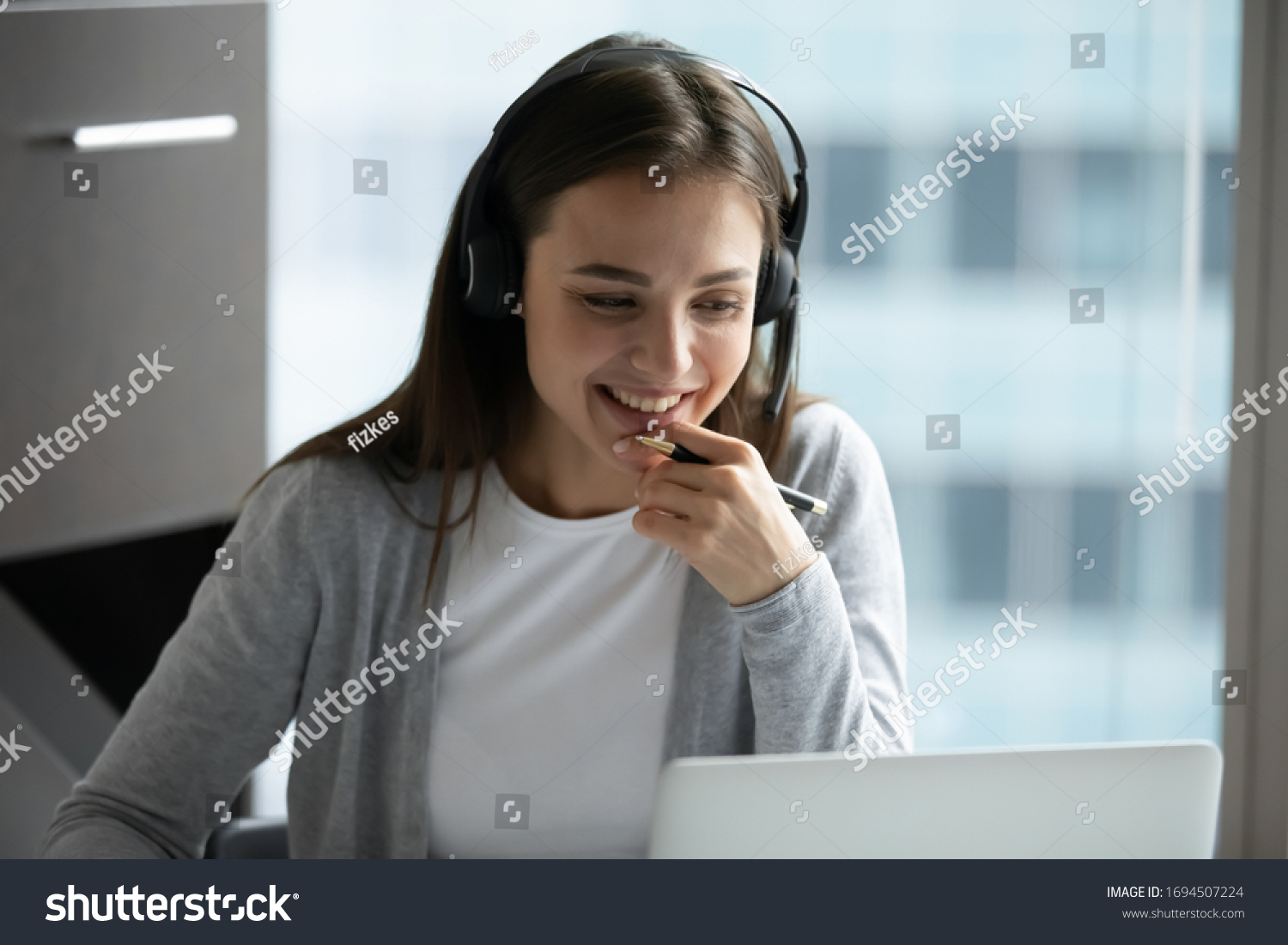 Happy millennial female in headphones watch webinar on laptop in modern office, smiling young businesswoman have fun laugh talk on video call with client or colleague use wireless Internet connection #1694507224