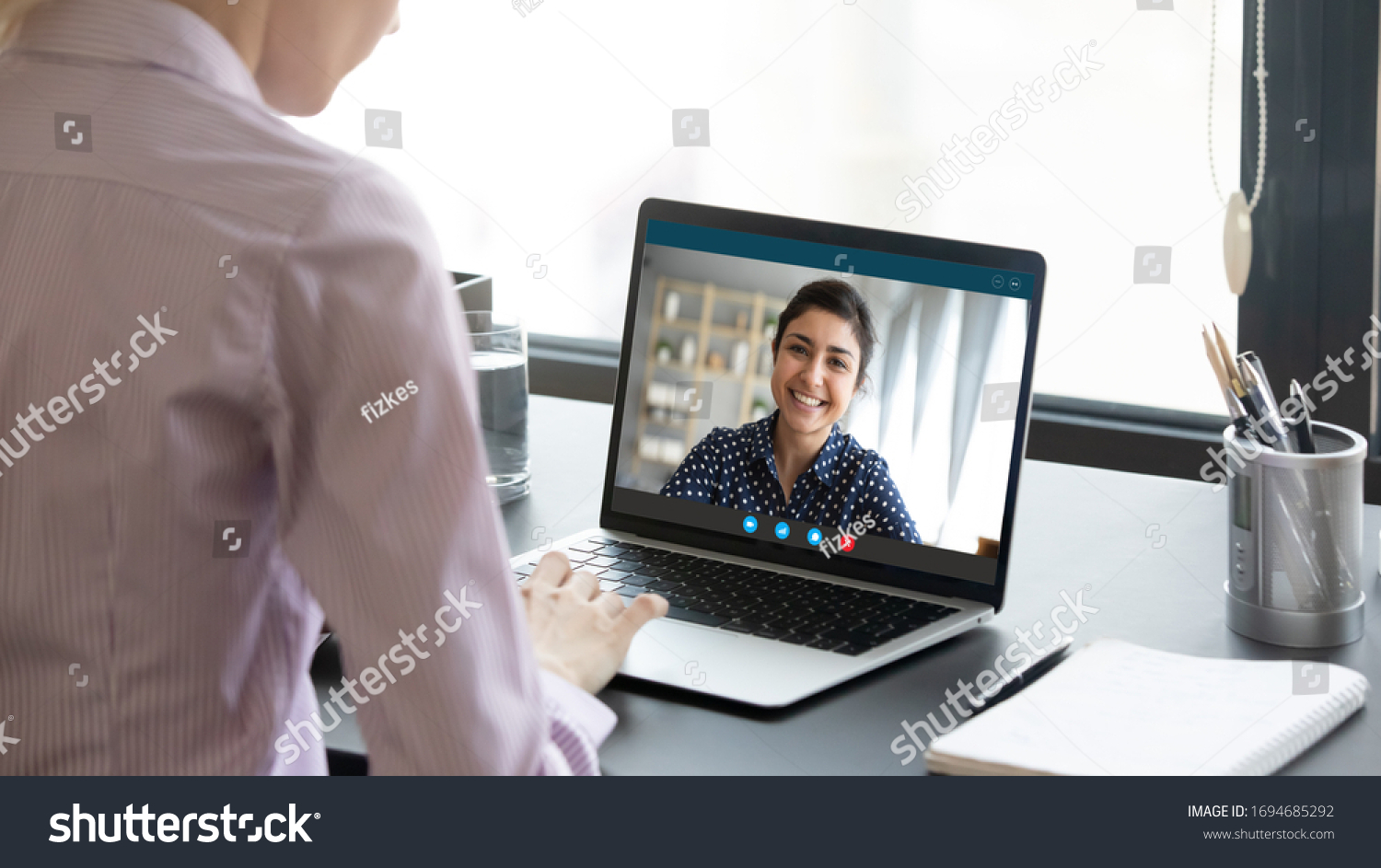 Indian girl communicate with friend on-line by video call, pc screen view over female shoulder. Mental health expert online therapy, colleagues work on common project use videoconferencing app concept #1694685292