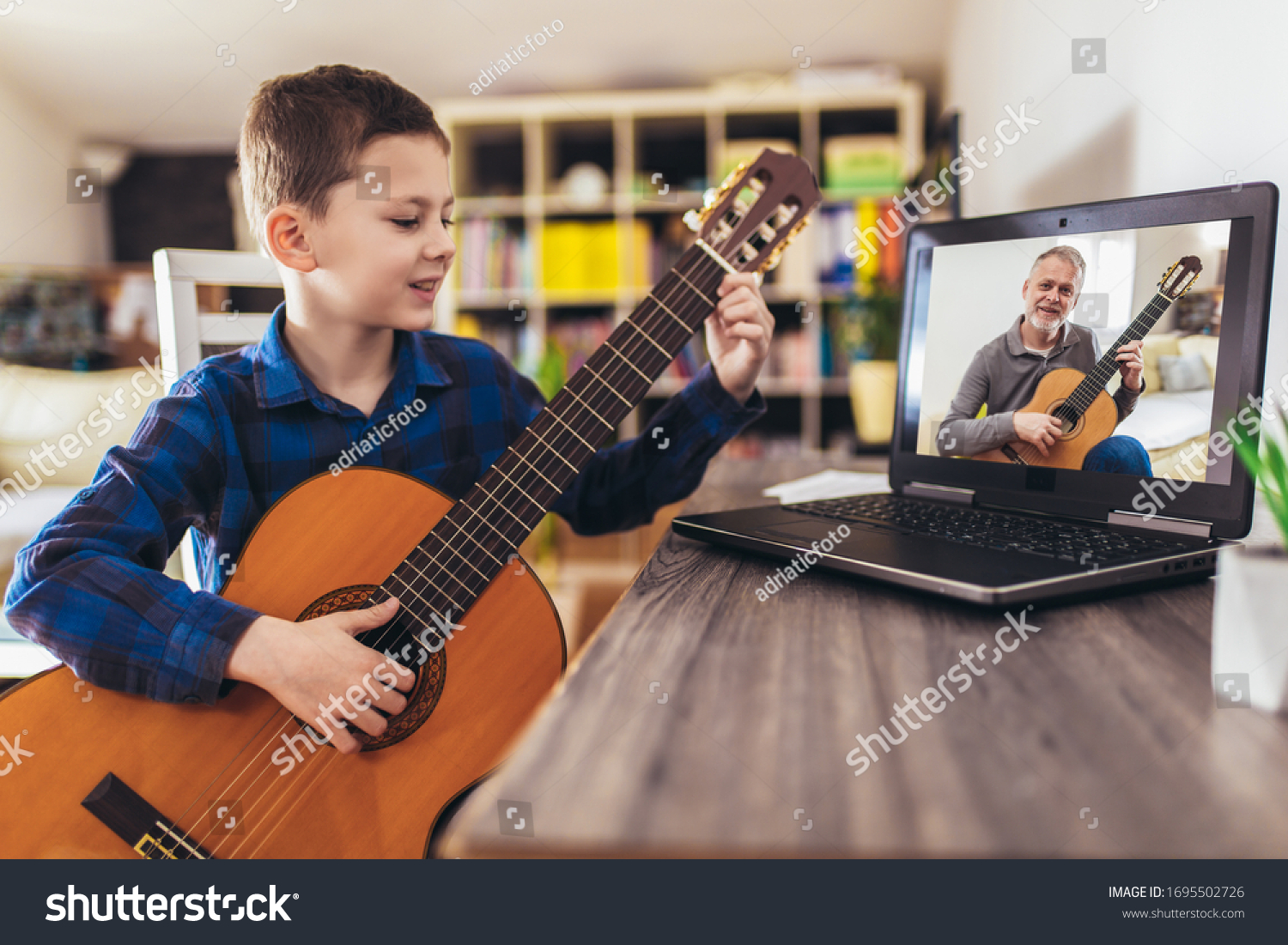 Focused boy playing acoustic guitar and watching online course on laptop while practicing at home. Online training, online classes. #1695502726