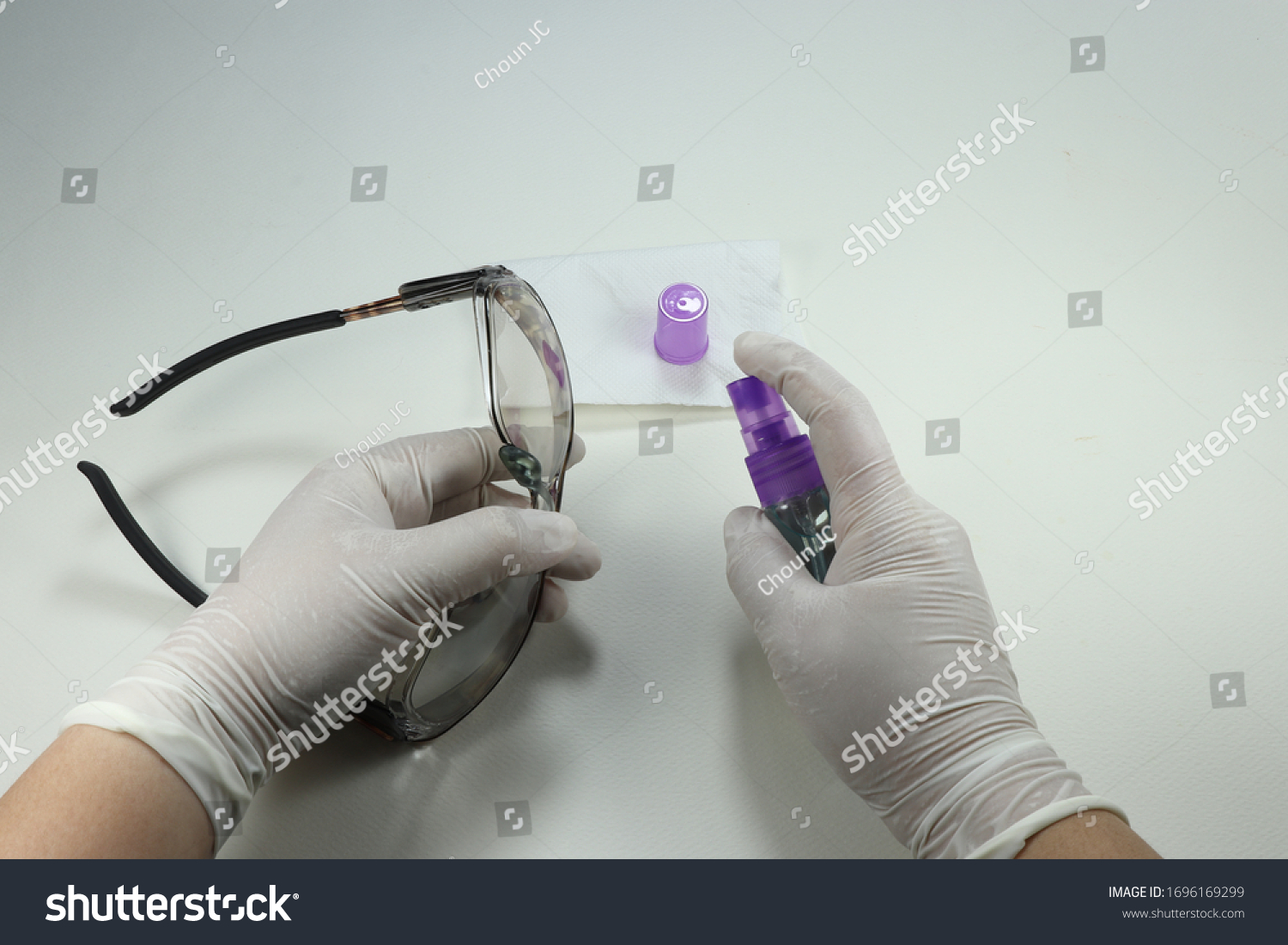 Staff wearing medical glove and cleaning protection glasses with alcohol spray. Avoid infected corona virus and bacteria from touching public object.   #1696169299