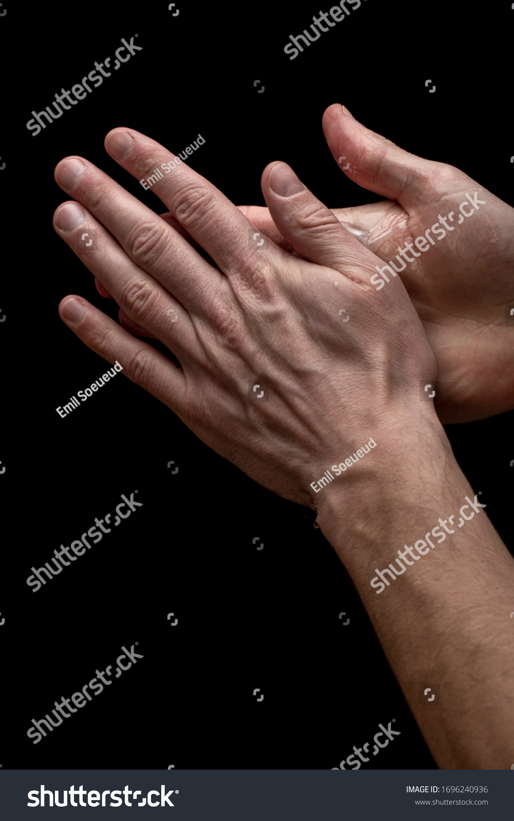 Young man is washing his hands with bubly soap on his hands on a black background, closeup #1696240936