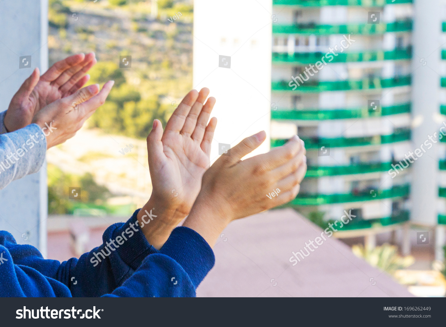 Family applauding medical staff from their balcony. People in Spain clapping on balconies and windows in support of health workers during the Coronavirus pandemic #1696262449
