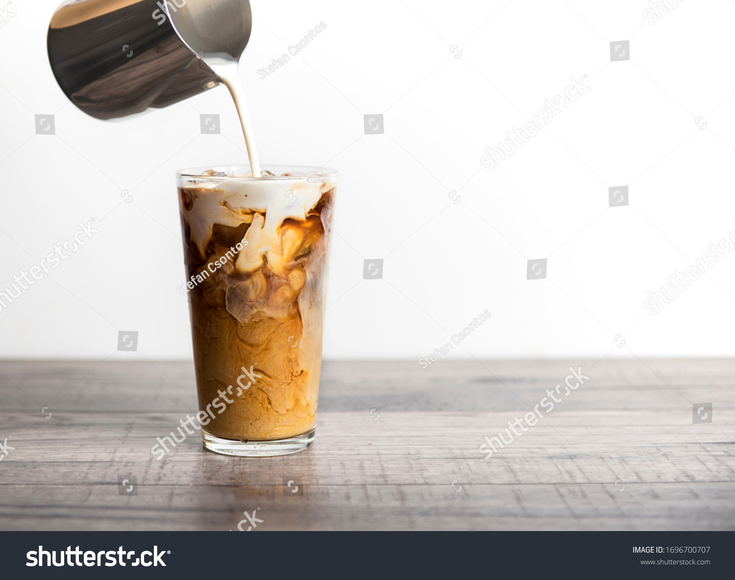 Ice coffee latte with cream being poured into it showing the texture and refreshing look of the drink, with a clean background. #1696700707
