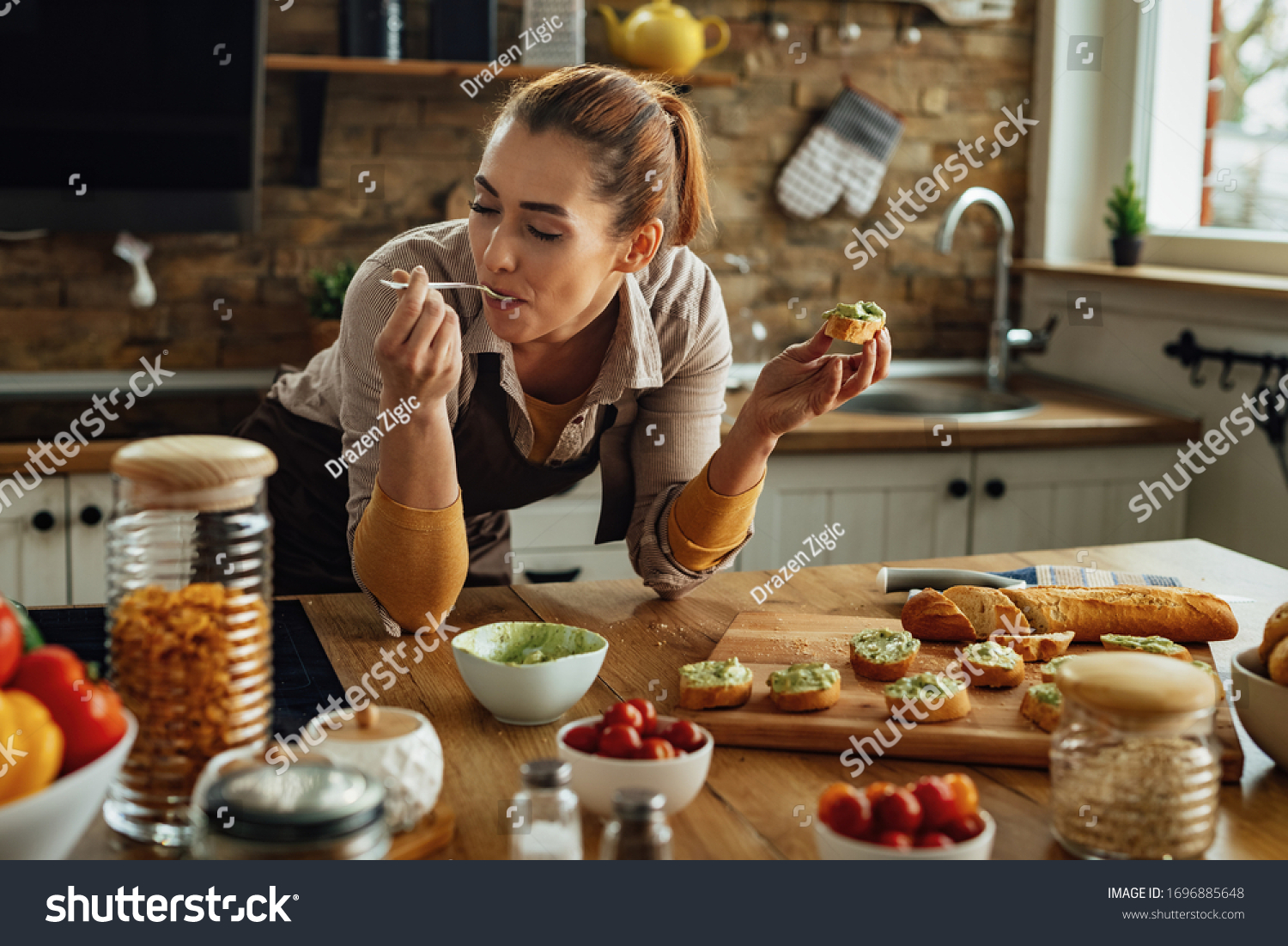 Smiling woman enjoying in taste of healthy food while making avocado bruschetta in the kitchen.  #1696885648