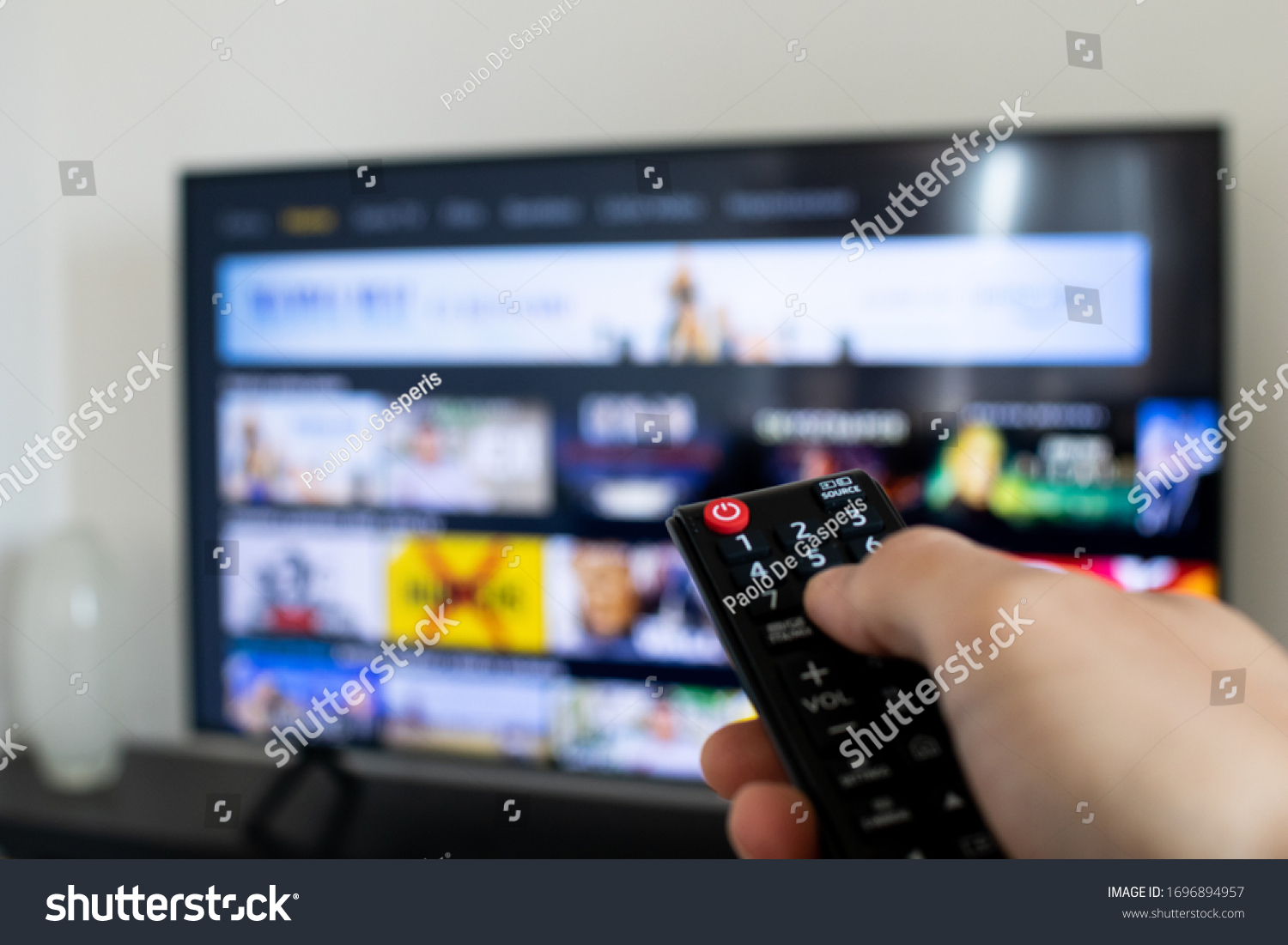 Tv remote controller in hand of customer looking for some content in Smart Tv app for streaming video. Watching streaming services for entertainment on television. Choosing TV series and movies #1696894957