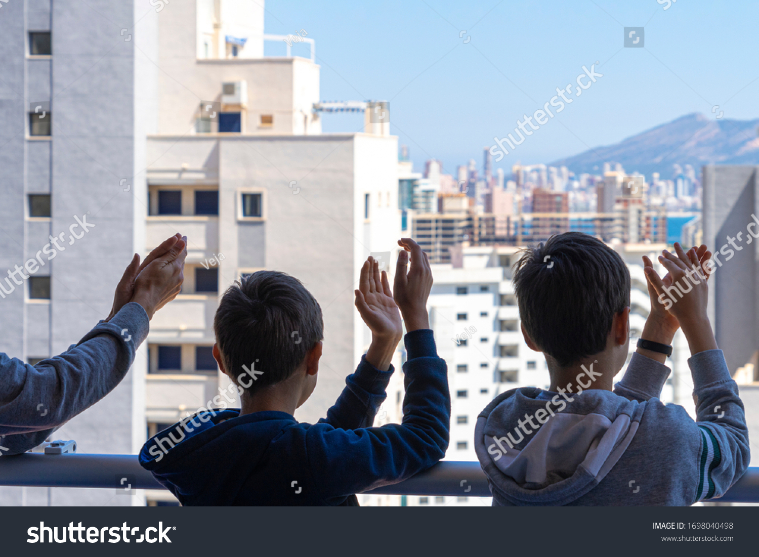 Family applauding medical staff from their balcony. People in Spain clapping gratitude on balconies and windows in support of health workers, doctors and nurses during the Coronavirus pandemic #1698040498