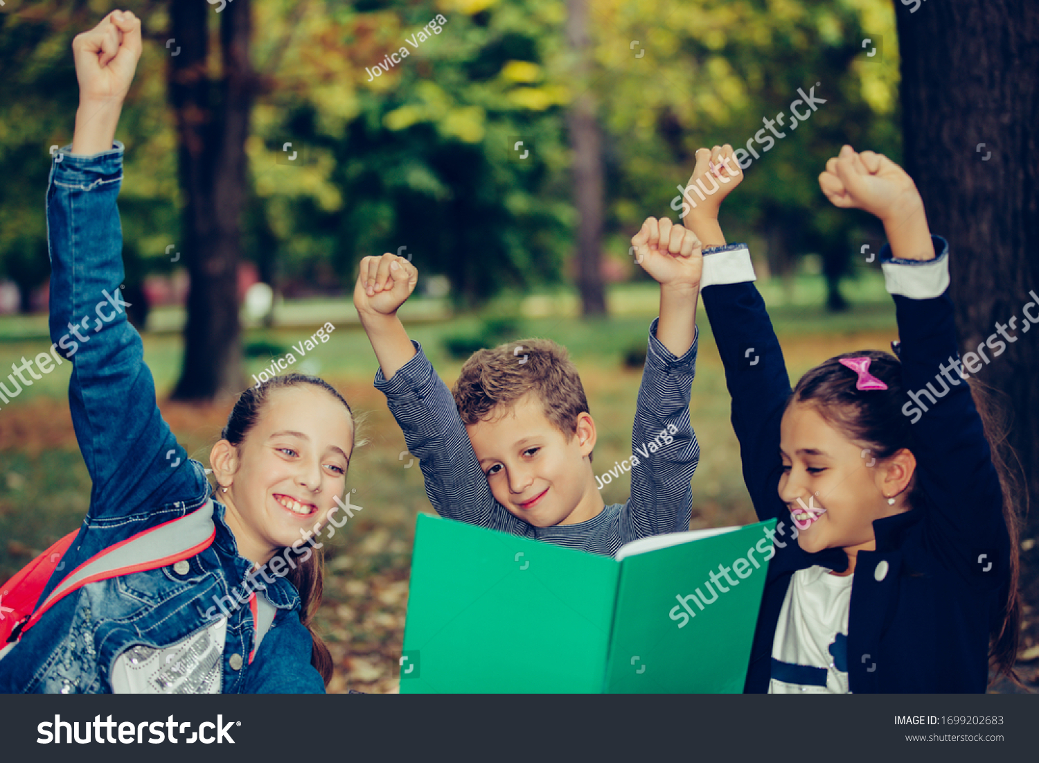 Happy little children celebrating success with raising hands. Three happy kids celebrating excellent results on a test at school. Selective focus #1699202683