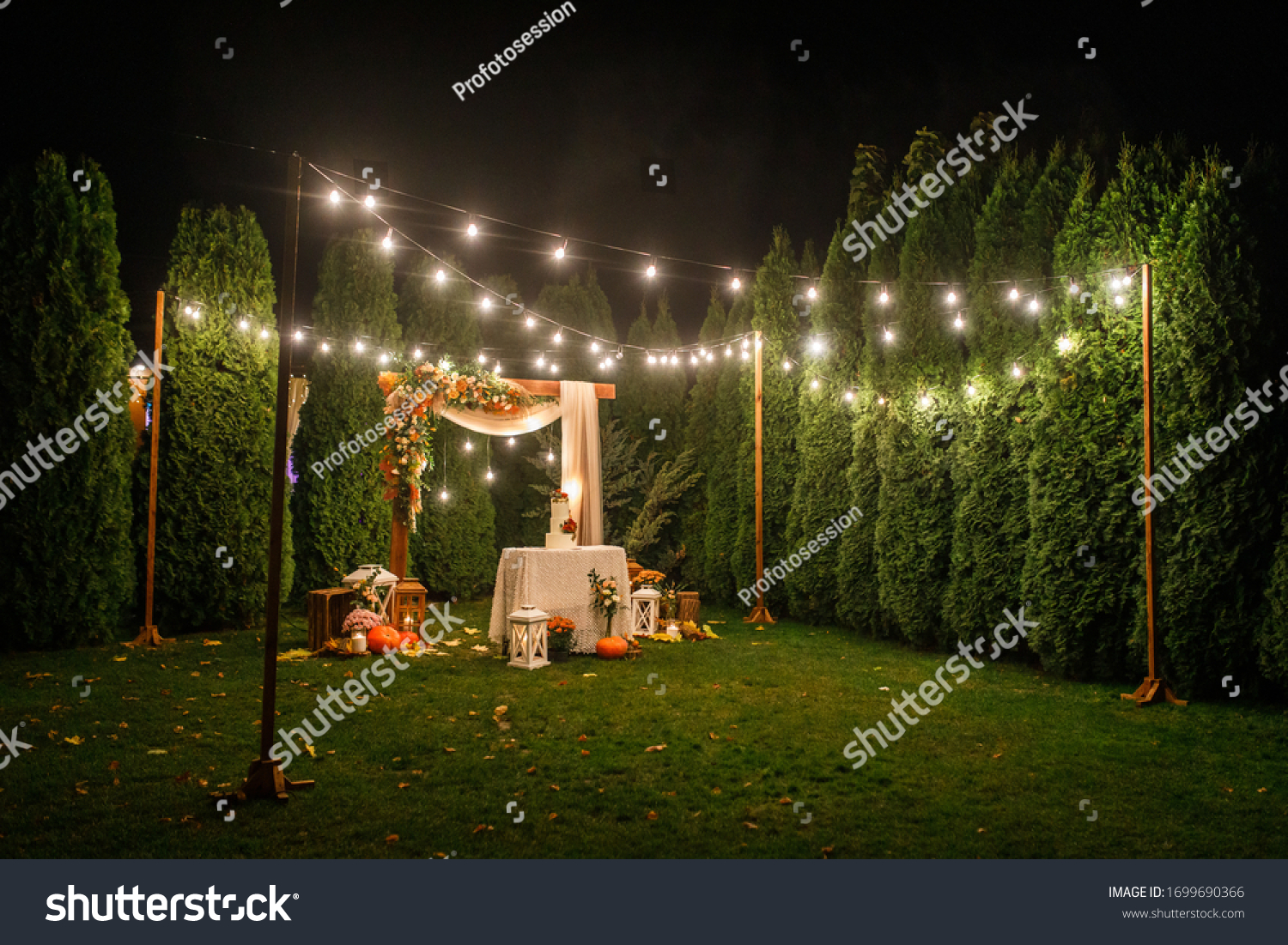 night wedding ceremony, the arch is decorated with flowers, candles and garlands of light bulbs and there is a wedding cake on the table #1699690366