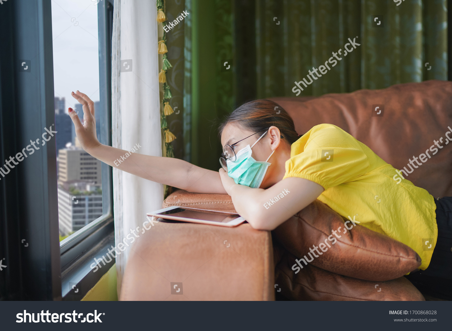 Young asian woman isolating at home with tablet on the sofa in the living room. She is bored because stay at home campaign for coronavirus prevention. #1700868028