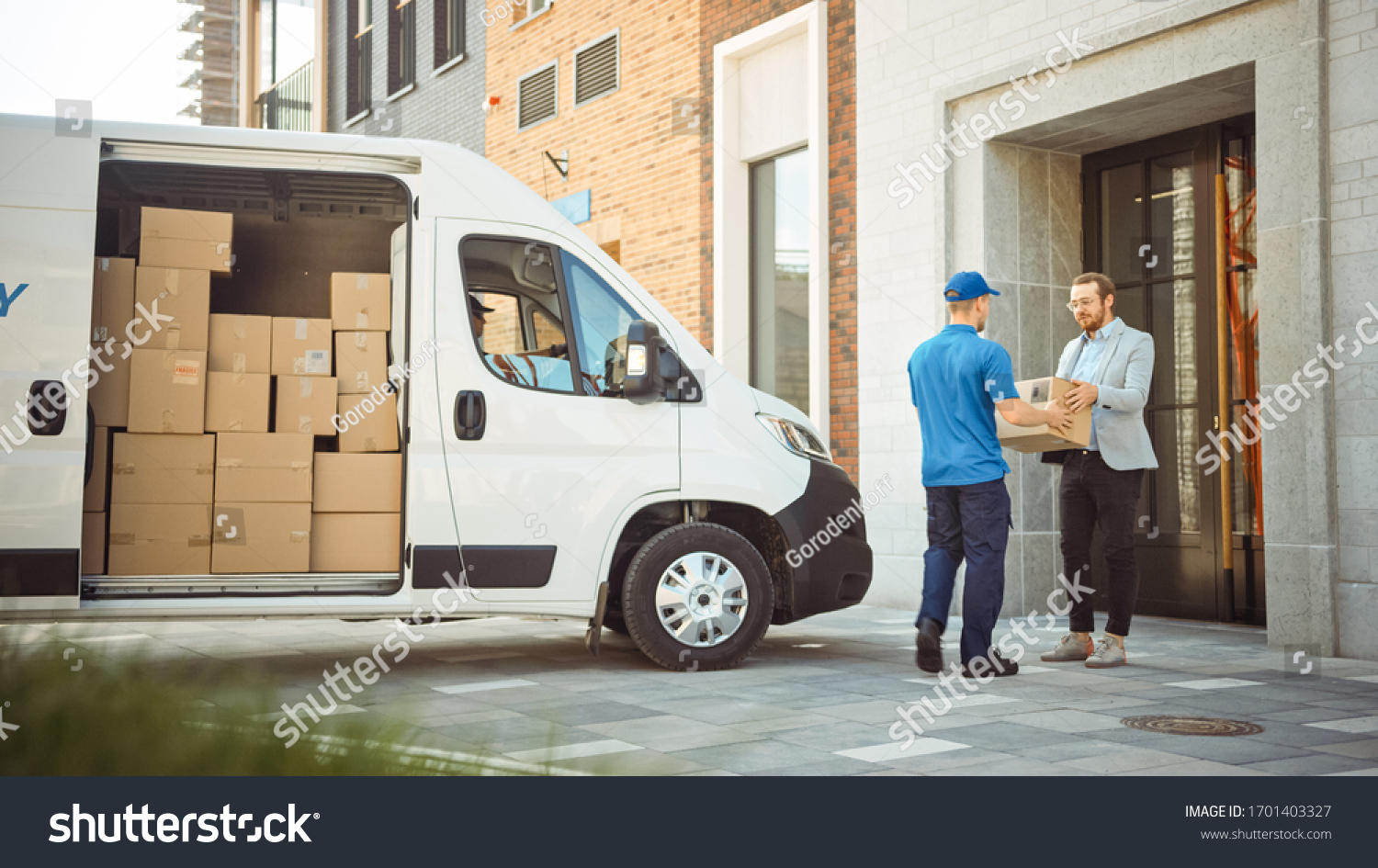 Delivery Man Gives Postal Package to a Business Customer, Who Signs Electronic Signature POD Device. In Stylish Modern Urban Office Area Courier Delivers Cardboard Box Parcel to a Man. #1701403327