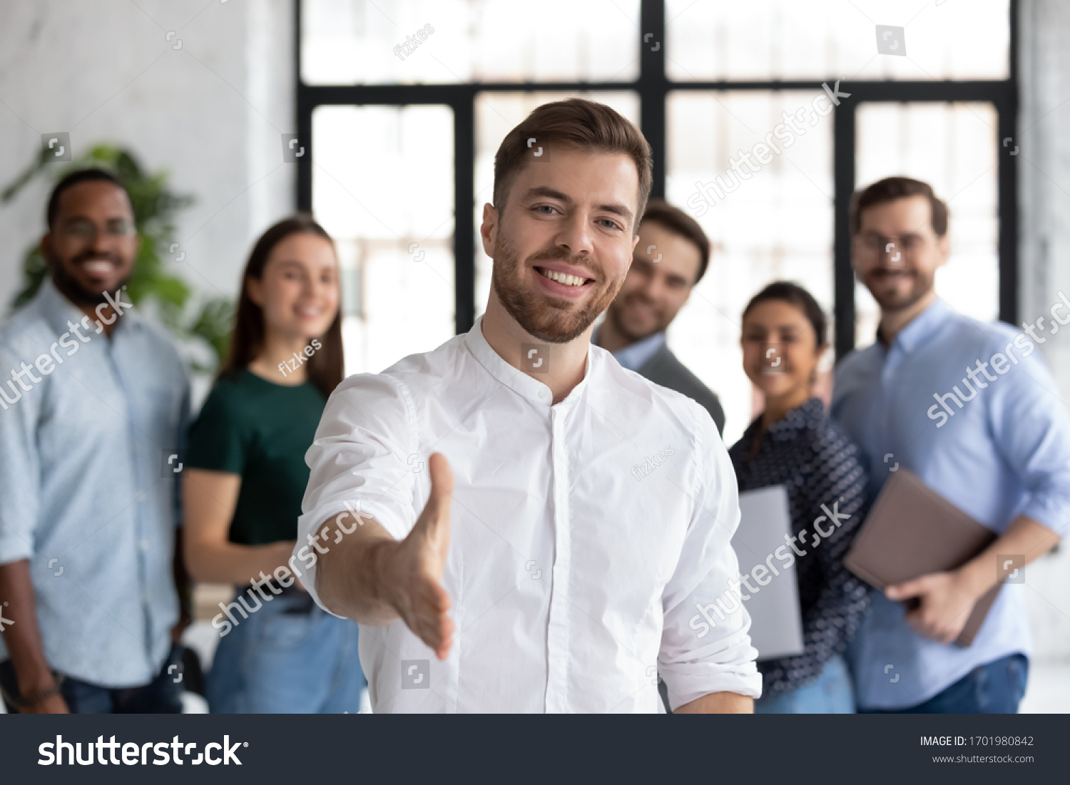 Smiling young Caucasian businessman stretch hand greeting meeting with new office employee or worker, happy male team leader or employer welcome newcomer or intern at workplace, recruitment concept #1701980842
