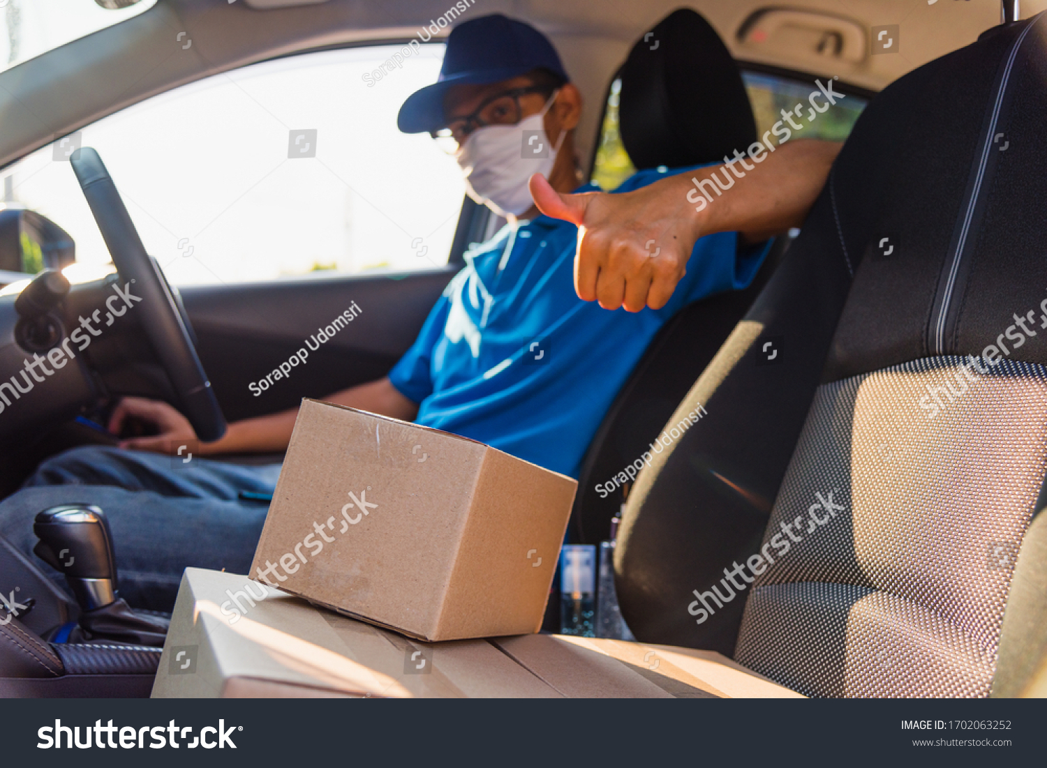 Asian Young delivery man courier online with boxes with uniform sitting in driving car he protective face mask, service customer on front house under curfew quarantine pandemic coronavirus COVID-19 #1702063252