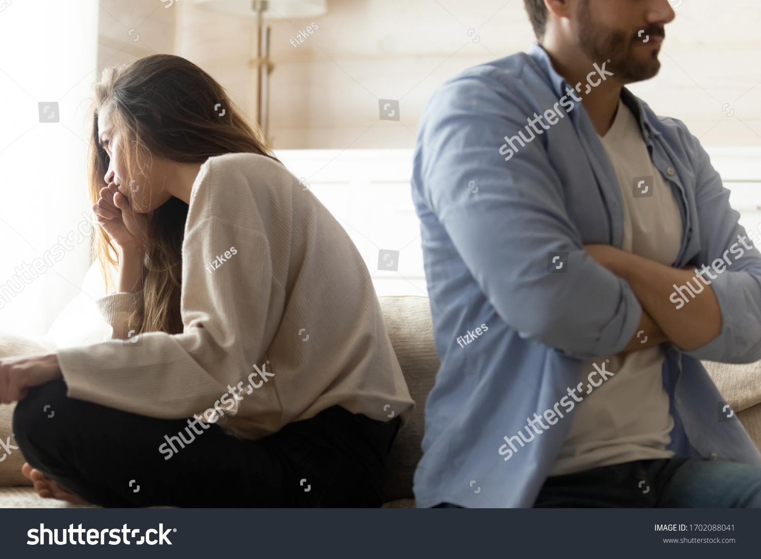 Stressed young married couple sitting separately on different sides of sofa, ignoring each other after quarrel. Offended spouses do not talk communicate, feeling depressed disappointed after argue. #1702088041