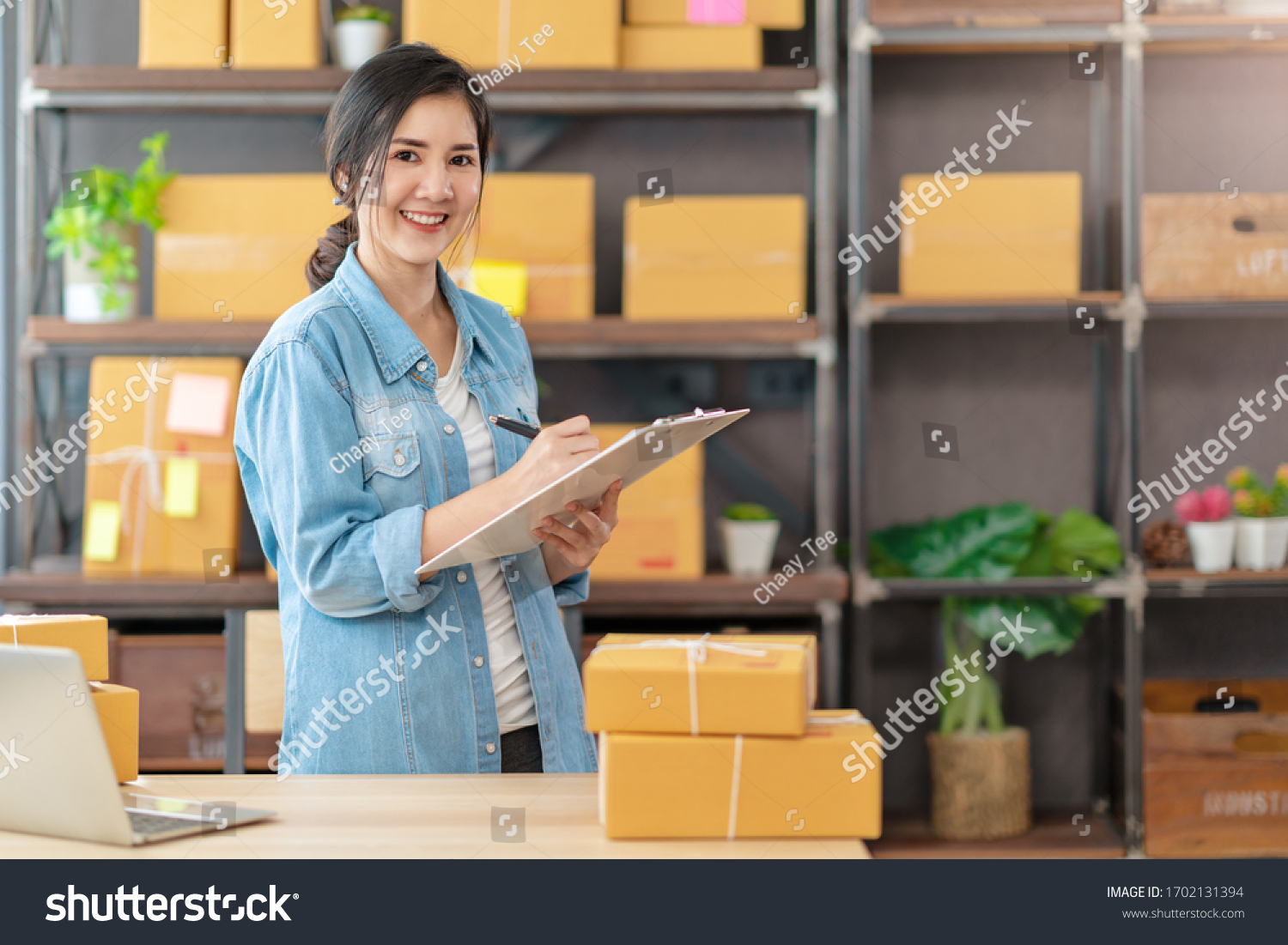 Young attractive asian woman owner startup business look at camera work happy with box at home prepare parcel delivery in sme supply chain, procurement, omnichannel or coronavirus quarantine concept. #1702131394