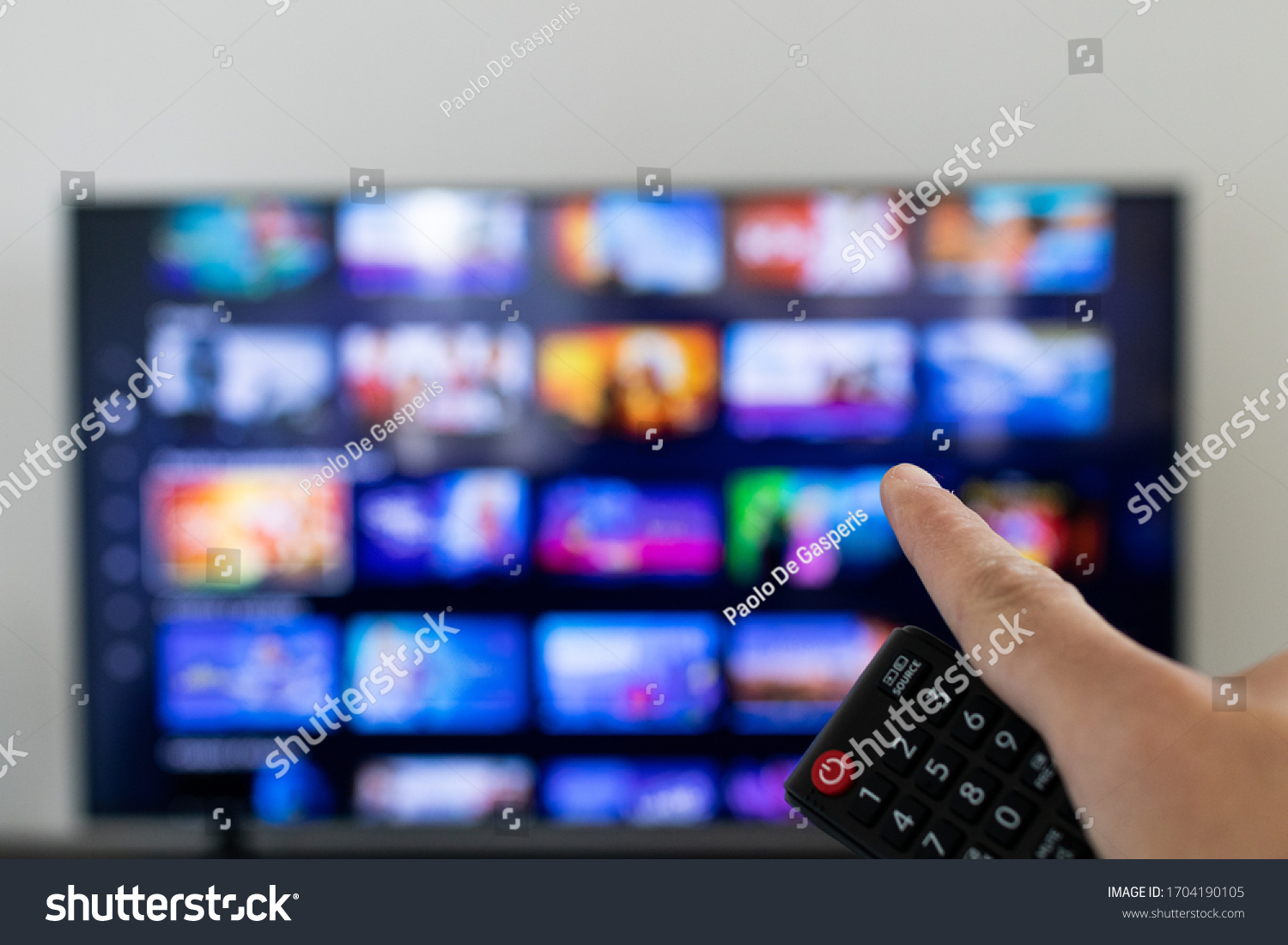 Remote controller and tv blurred in background. Video streaming service catalogue in grid blurred on smart TV.  #1704190105