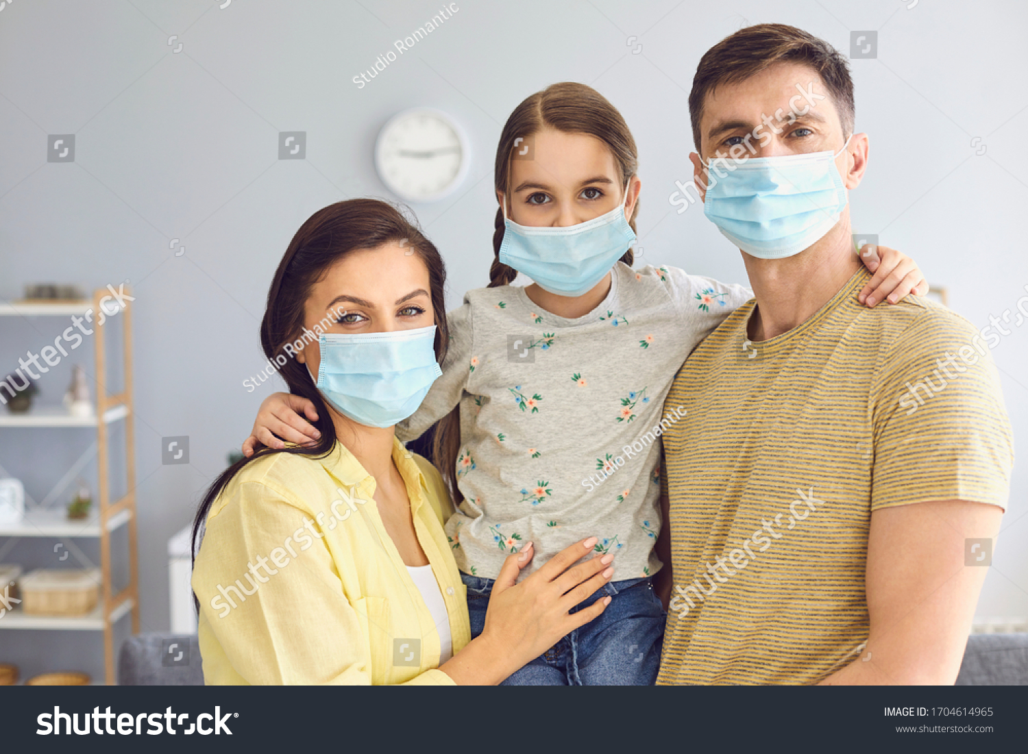 Family in medical masks on the face looks at the camera while standing in the room at home. #1704614965