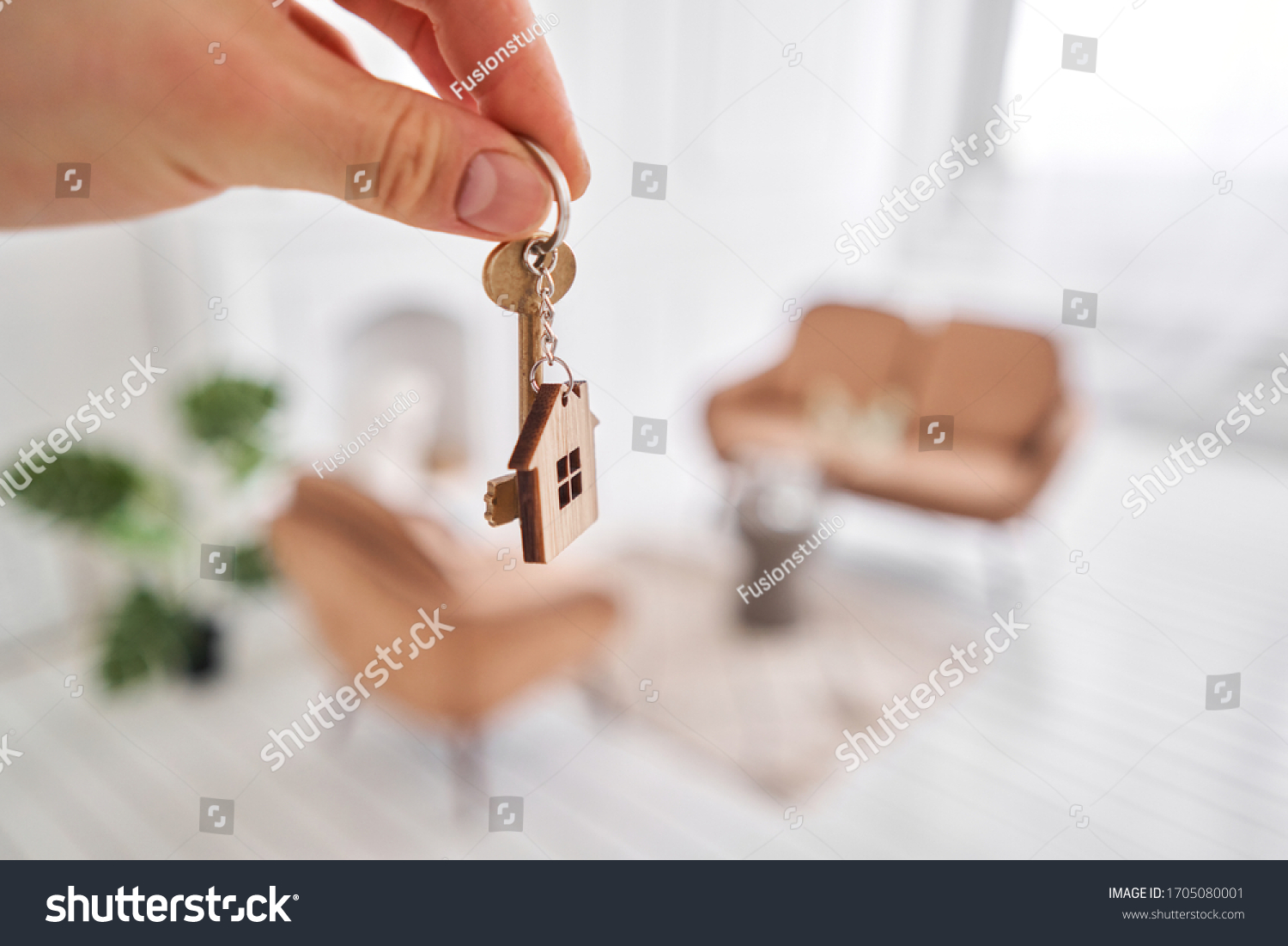 Men hand holding key with house shaped keychain. Modern light lobby interior. Mortgage concept. Real estate, moving home or renting property. #1705080001