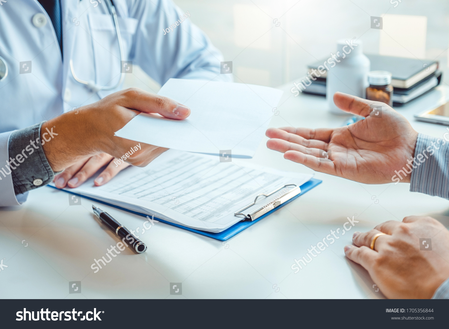 Doctor or physician writing diagnosis and giving a medical prescription to male Patient #1705356844