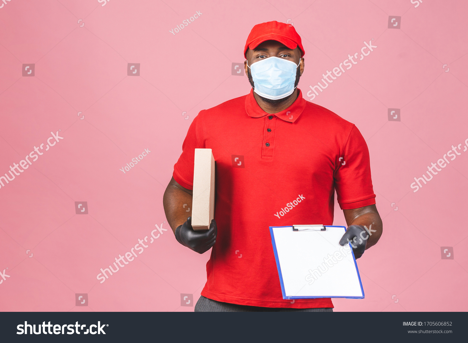 Delivery man employee in red cap blank t-shirt uniform face mask gloves hold empty cardboard box isolated on pink background. Service quarantine pandemic coronavirus virus 2019-ncov concept. #1705606852