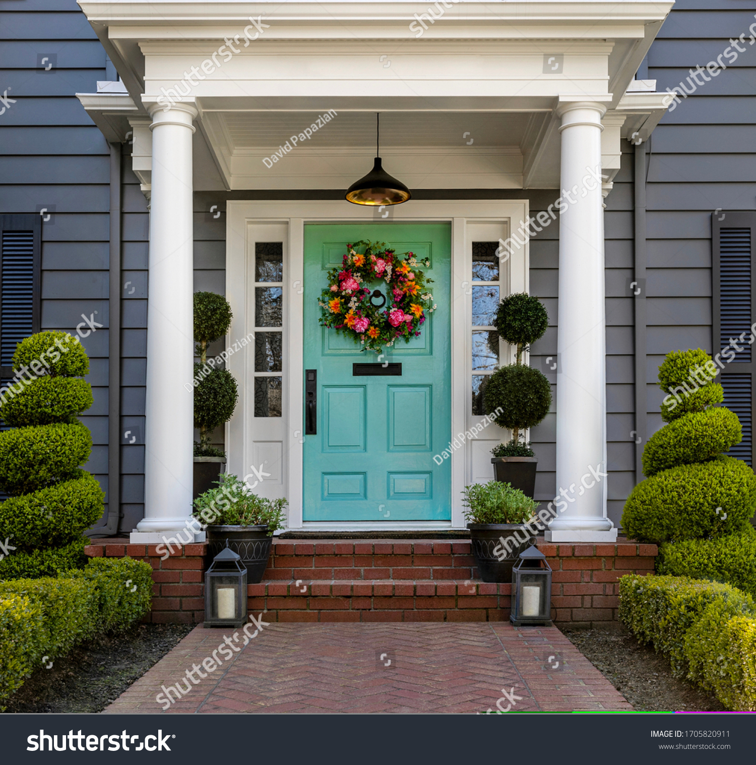 Beautifully decorated turquoise colored front door of traditional home. Brick path and trimmed hedges. #1705820911
