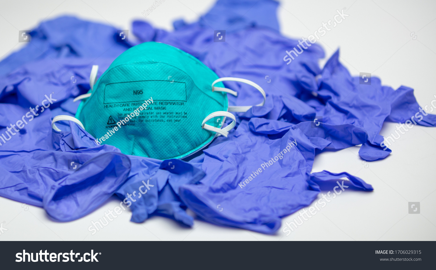 A turquoise N95 particulate respirator and surgical mask on top of many medical gloves. #1706029315