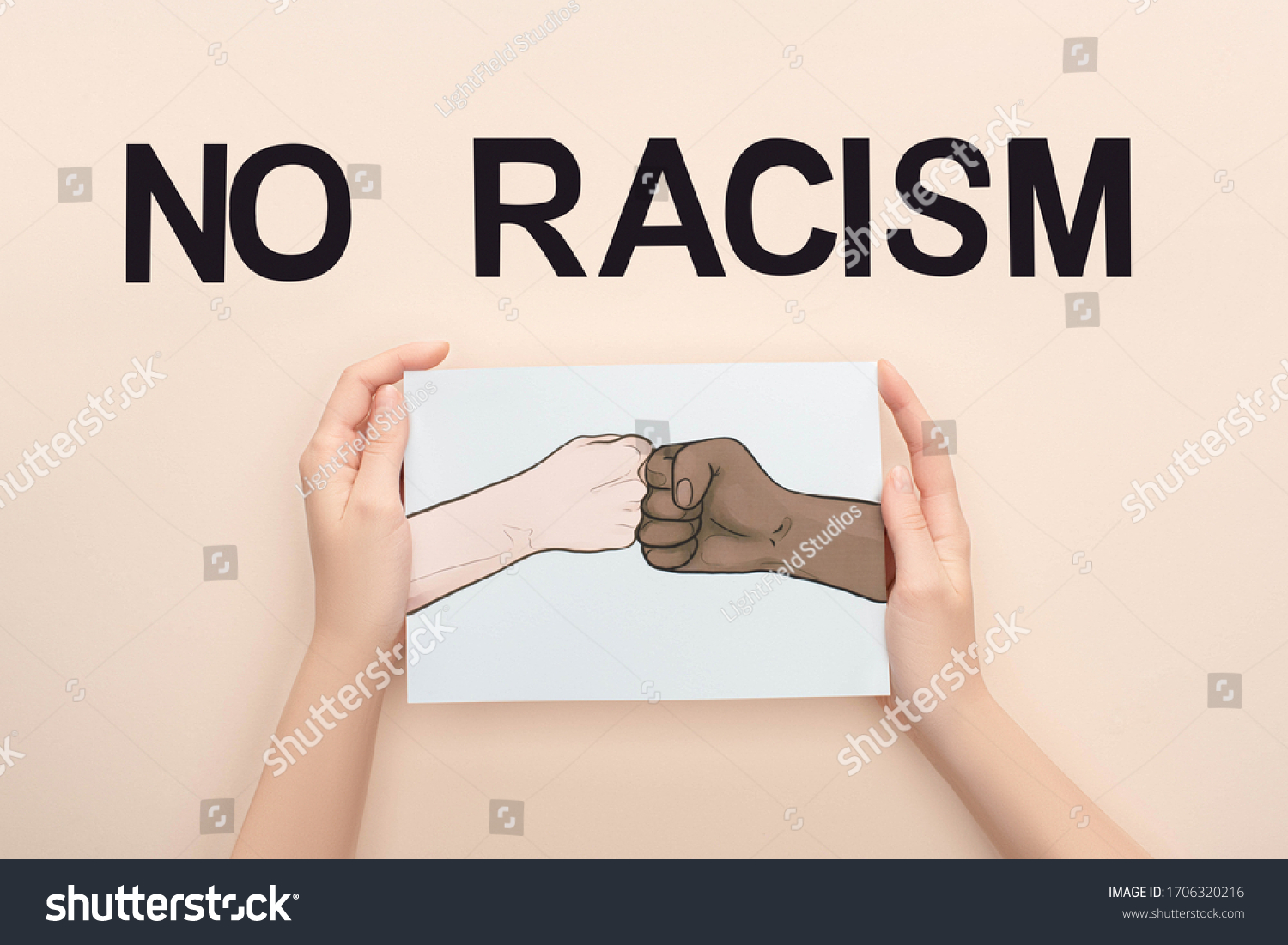 cropped view of woman holding picture with drawn multiethnic hands doing fist bump near no racism lettering on beige background #1706320216