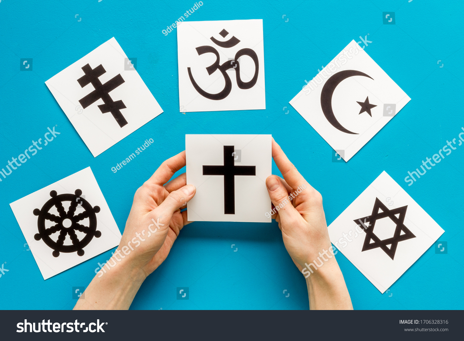 Choose religion concept. Hand with catholic cross near world religions symbols on blue background top view #1706328316