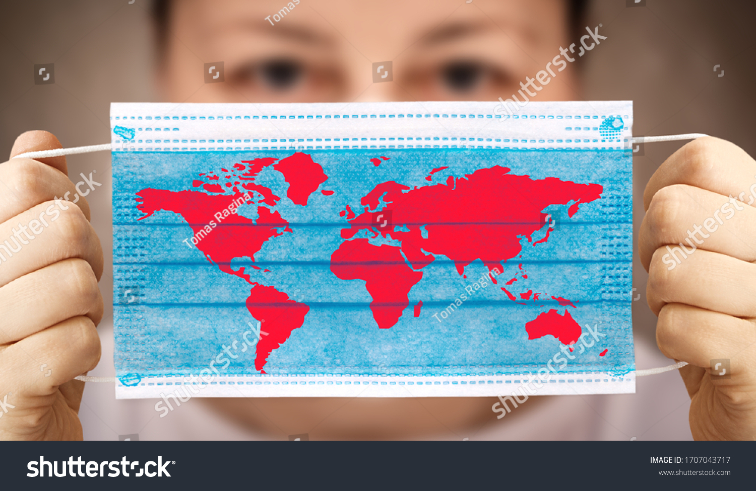 Face mask in hand with world map. Covid-19 outbreak around the world. The global economic crisis. Crash by coronavirus. Life in lockdown around the world #1707043717