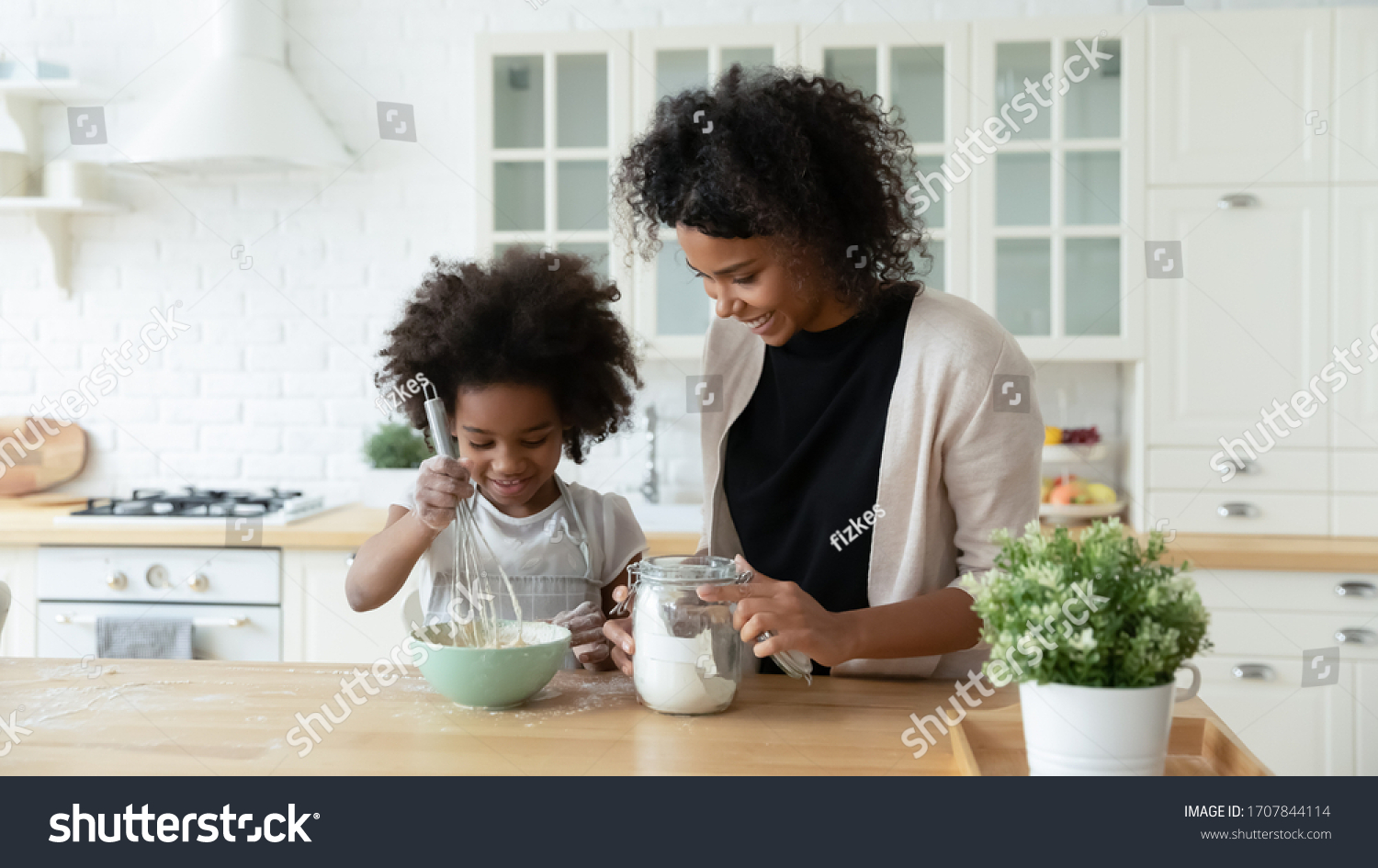 Loving young African American mother teach small biracial daughter bake in kitchen, happy caring ethnic mom and little girl child preparing pancakes or biscuits, make breakfast at home together #1707844114