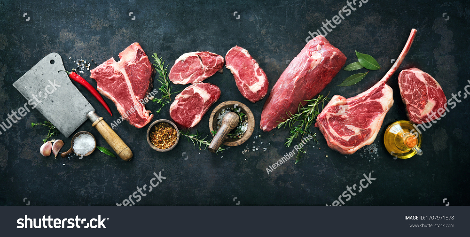Variety of raw beef meat steaks for grilling with seasoning and utensils on dark rustic board #1707971878
