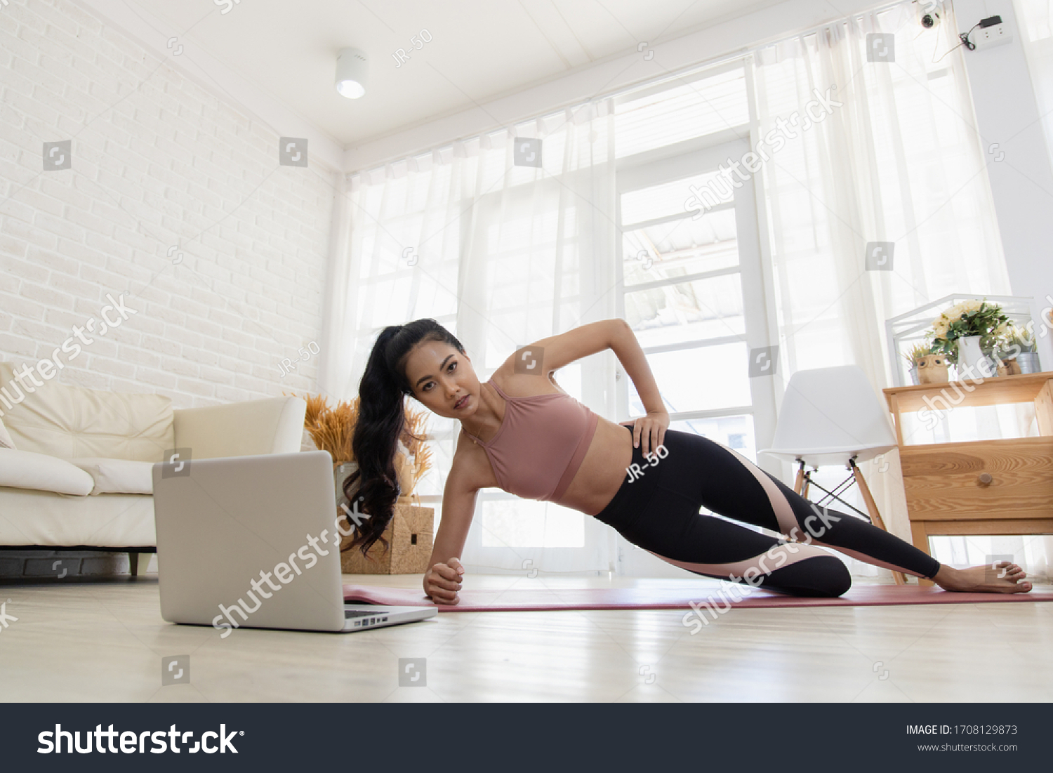 A beautiful Asian woman's fitness at home instead of going to the gym. Her learning new exercises watching online workout tutorials over her computer laptop at home. Exercise concept for good shape #1708129873