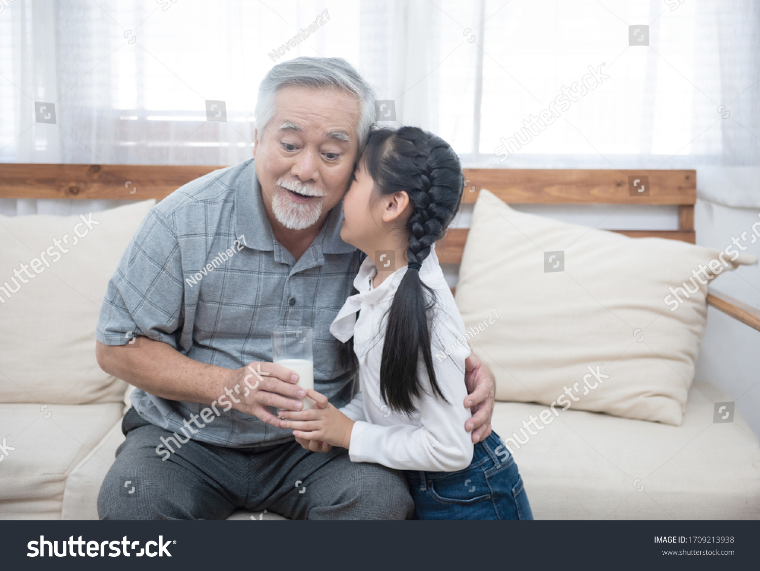 Happy asian senior elderly grandfather have grandchild look after and take care with giving milk and kiss on cheek while sitting on sofa at home,retirement health lifestyle concept. #1709213938