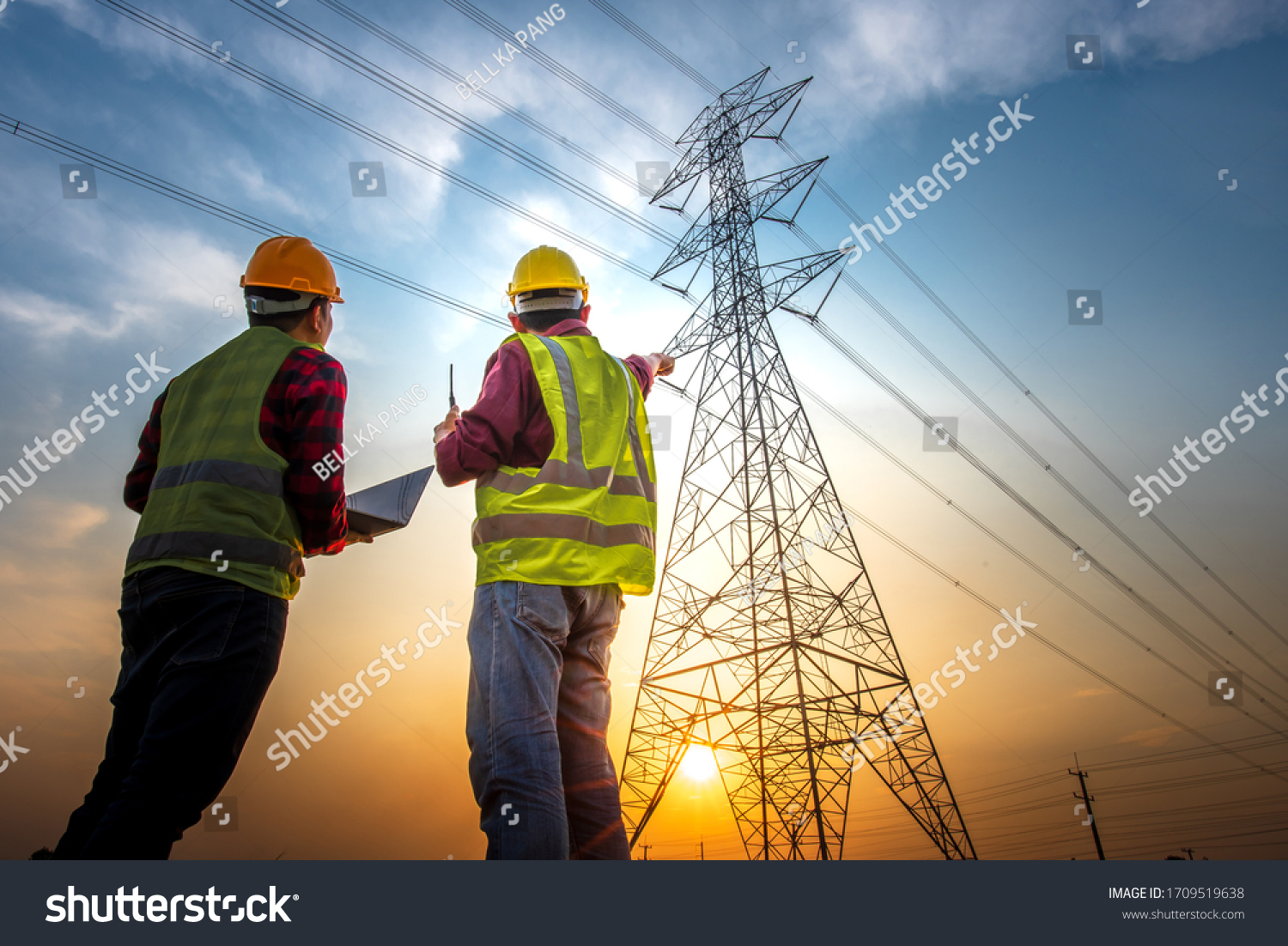 Picture of two electrical engineers using a notebook computer standing at a power station to view the planning work by producing electrical energy at high voltage electrodes. #1709519638