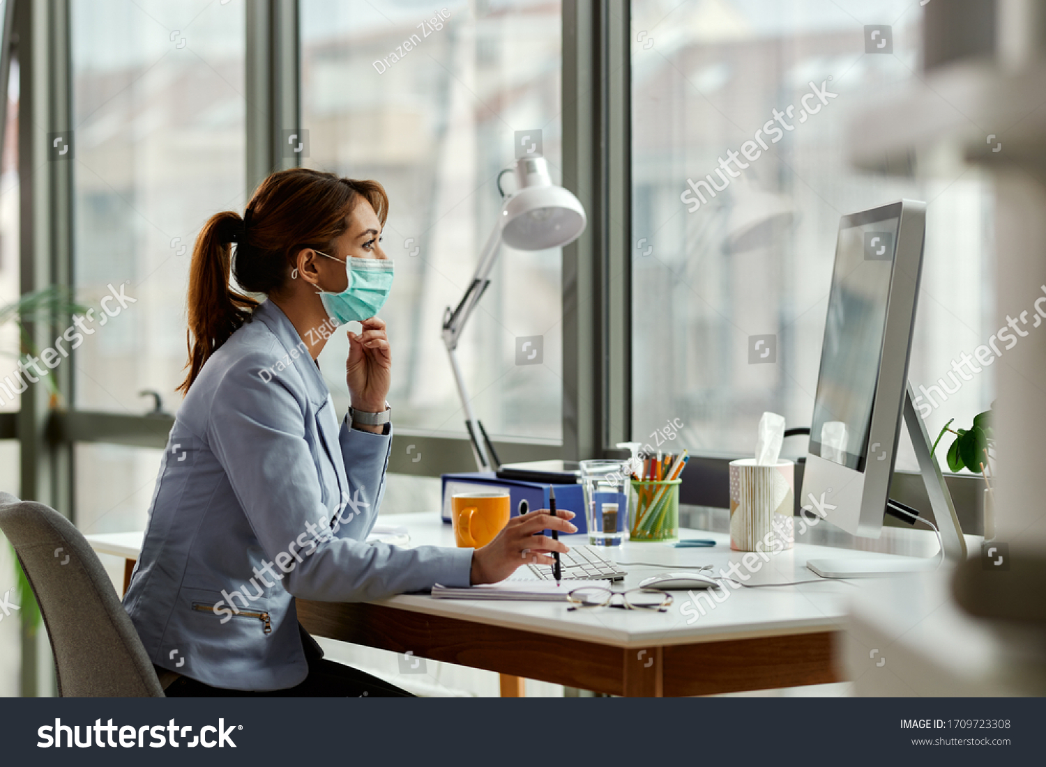 Young businesswoman wearing face mask while working on a computer in the office.  #1709723308