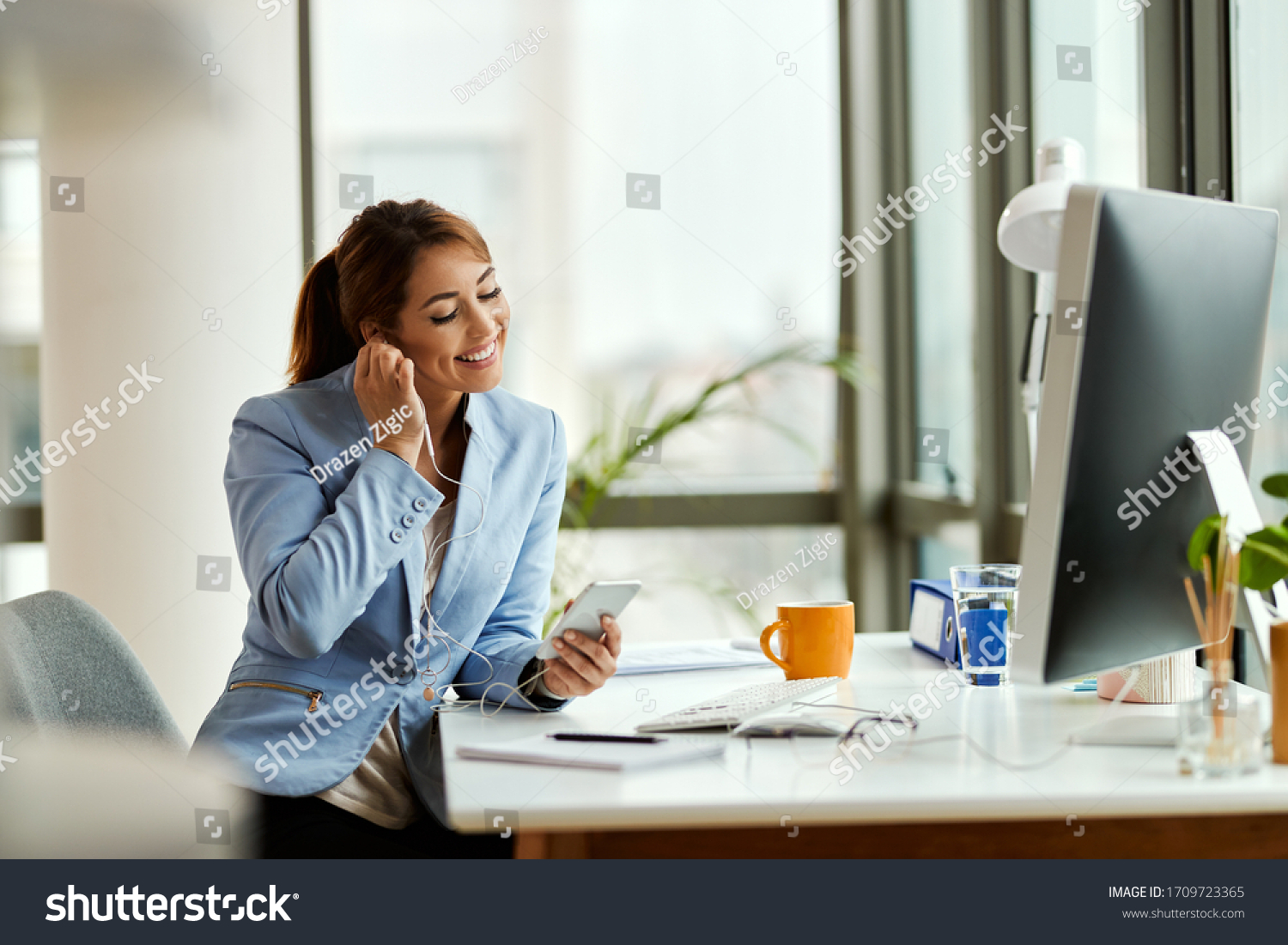 Young businesswoman relaxing while using mobile phone and listening music over earphones in the office. #1709723365