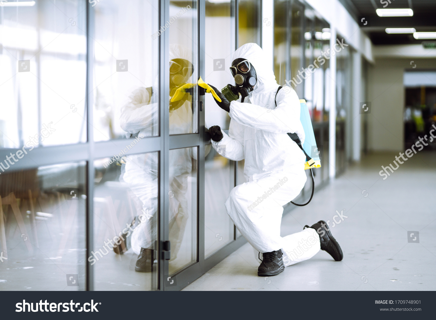 Man in protective hazmat suit washes door handles in office to preventing the spread of coronavirus, pandemic in quarantine city. Cleaning and disinfection of office. Covid-19. #1709748901