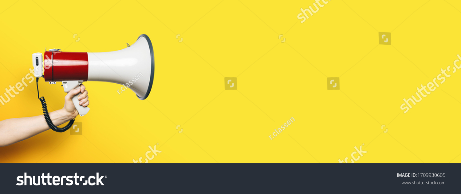 hand with a megaphone in front of an empty yellow background, banner size, with copyspace for your individual text. #1709930605