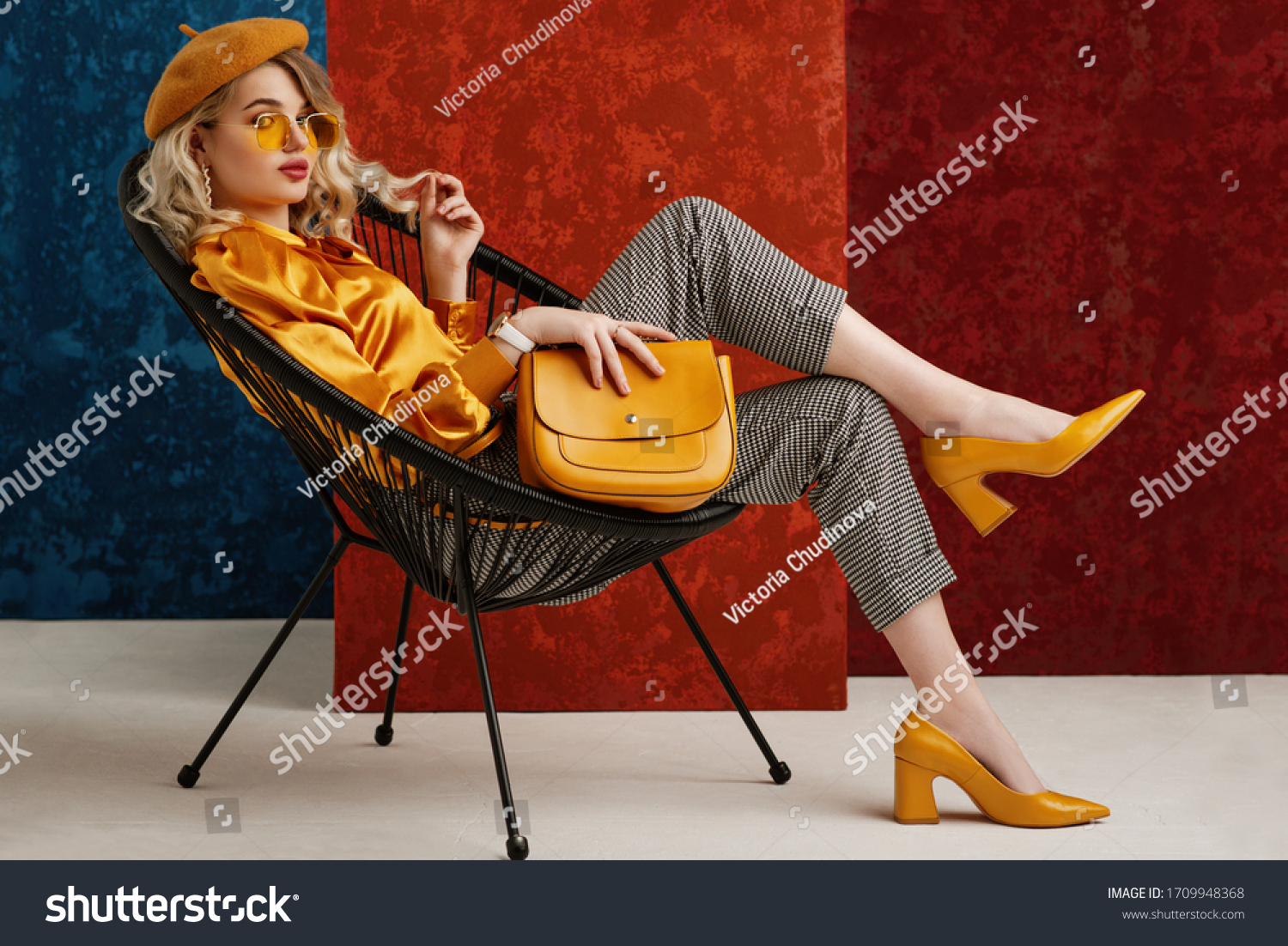 Full-length studio fashion portrait of elegant woman wearing yellow color sunglasses, beret, silk blouse, houndstooth printed trousers, pointed toe shoes, posing on chair, holding stylish leather bag
 #1709948368