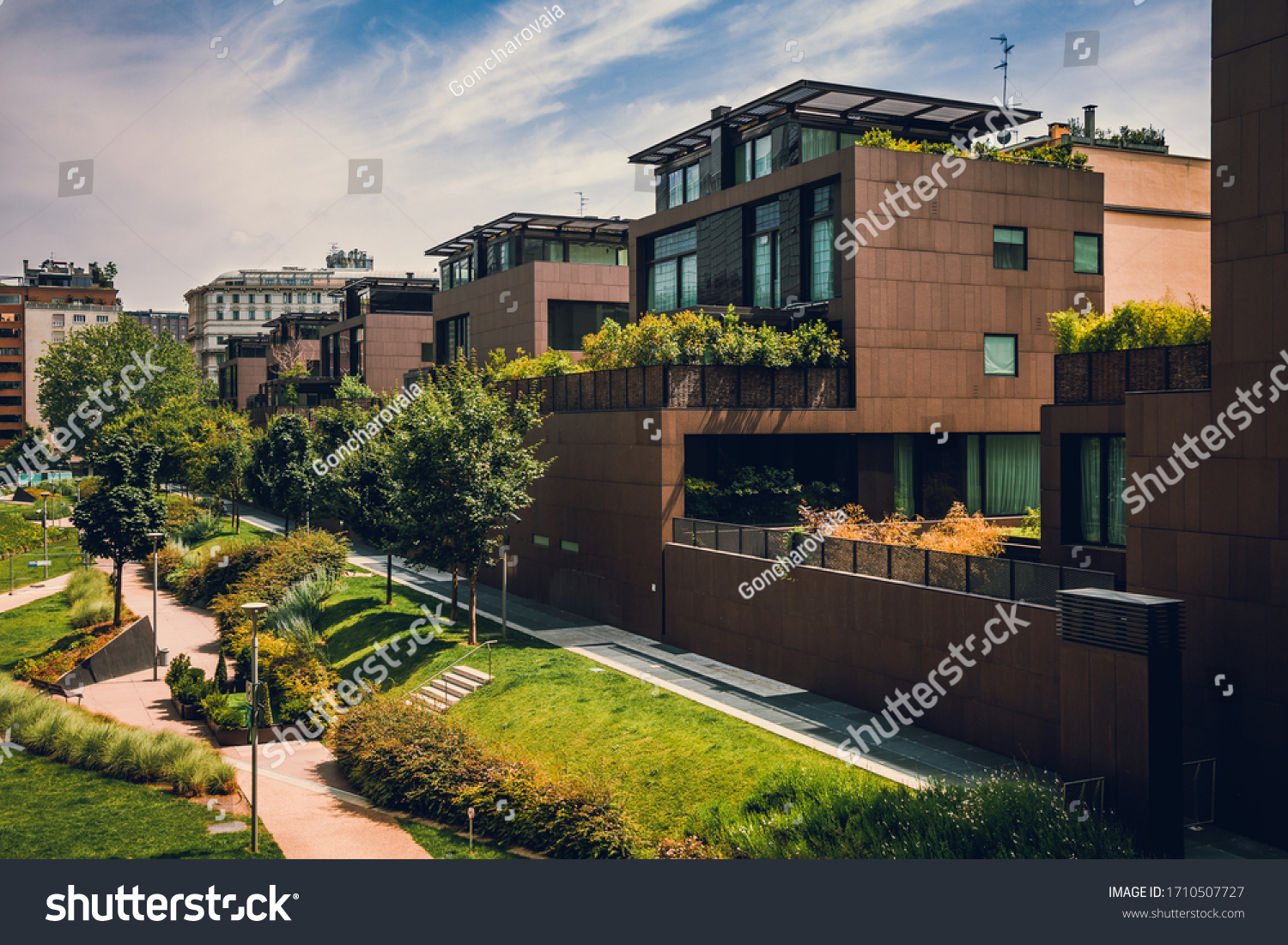 Modern residential buildings in the public green area. Apartment houses in Europe. Beautiful view of real estate homes in Milan, Italy. Business district in summer. Walking area with trees and grass. #1710507727