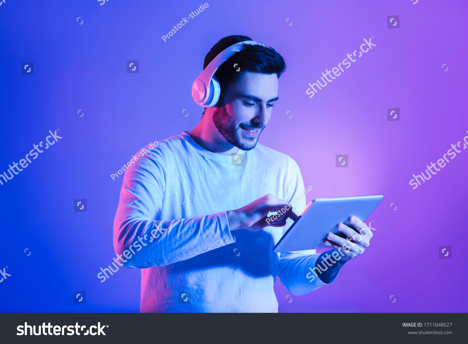 Modern gadgets for joy concept. Happy man in wireless headphones uses tablet #1711048627