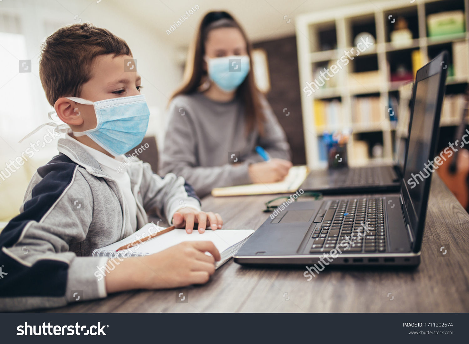 Boy and girl studies at home, wear protective masks, and doing school homework. Distance learning online education. #1711202674