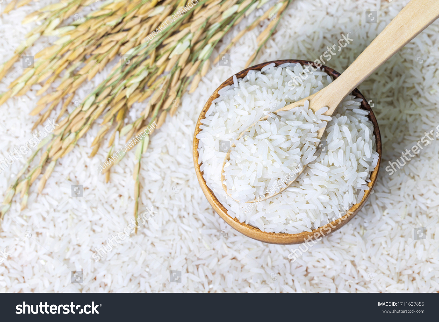 Top view of wooden spoon with rice on rice in wooden bowl on rice and rice ears background, Natural food high in protein
 #1711627855