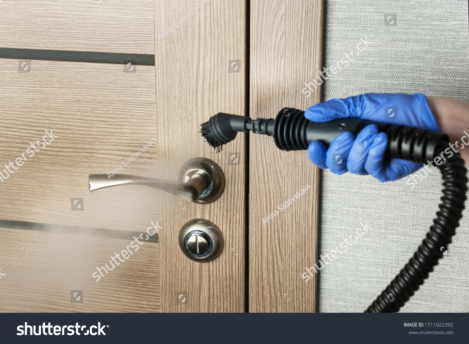 cleaning  door handle with steam generator, hand in blue glove holds steam genetator and hose with brush, which produces steam for disinfection from microbes, dirt and viruses, home cleaning concept #1711922392