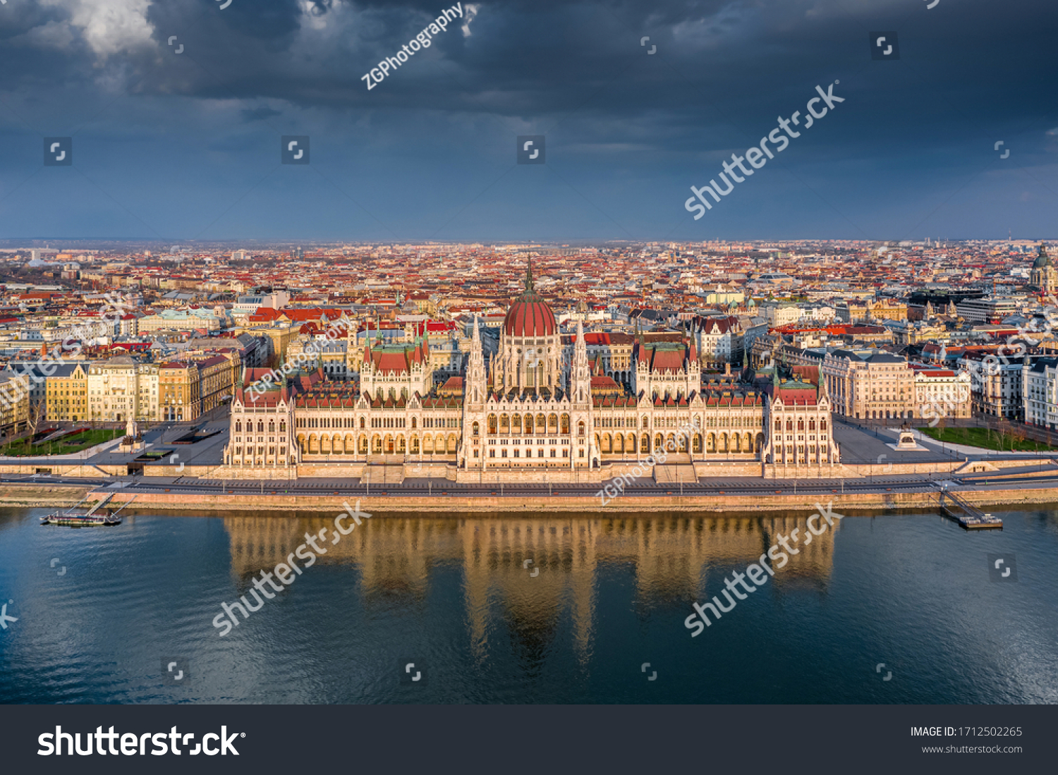 Budapest, Hungary - Aerial view of the beautiful Hungarian Parliament building with reflection and warm golden sunlight at sunset. The streets are totally empty due to the 2020 Coronavirus quarantine #1712502265