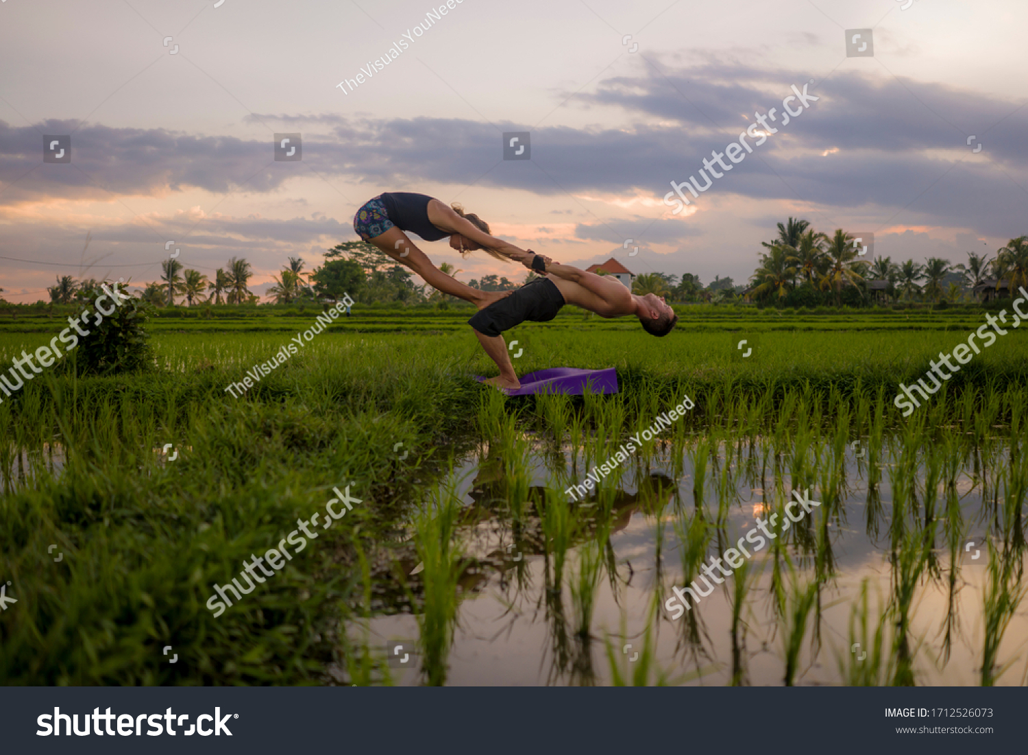 outdoors sunset acroyoga workout silhouette- young happy and fit couple practicing acro yoga drill at beautiful rice field enjoying nature and healthy lifestyle doing acrobatic pose  #1712526073