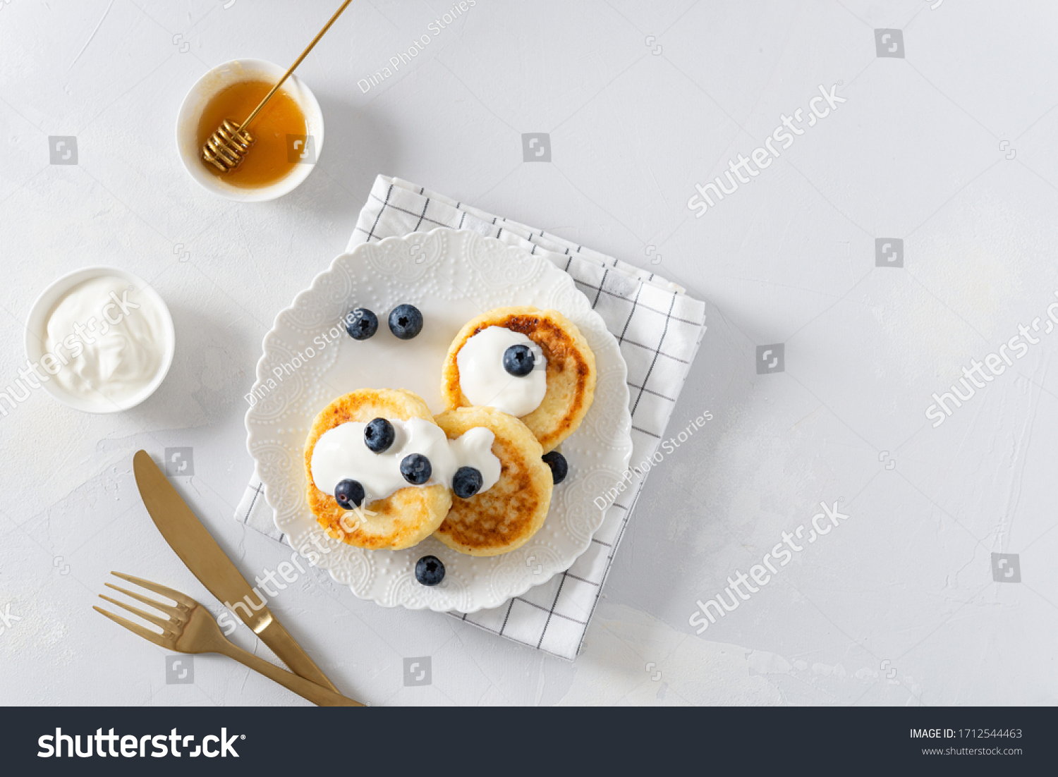 Cottage cheese pancakes on a white background. Syrniki with fresh blueberries. Pancakes with cottage cheese on a white board sprinkled with powdered sugar. Homemade food. Recipe. Copy space for text #1712544463