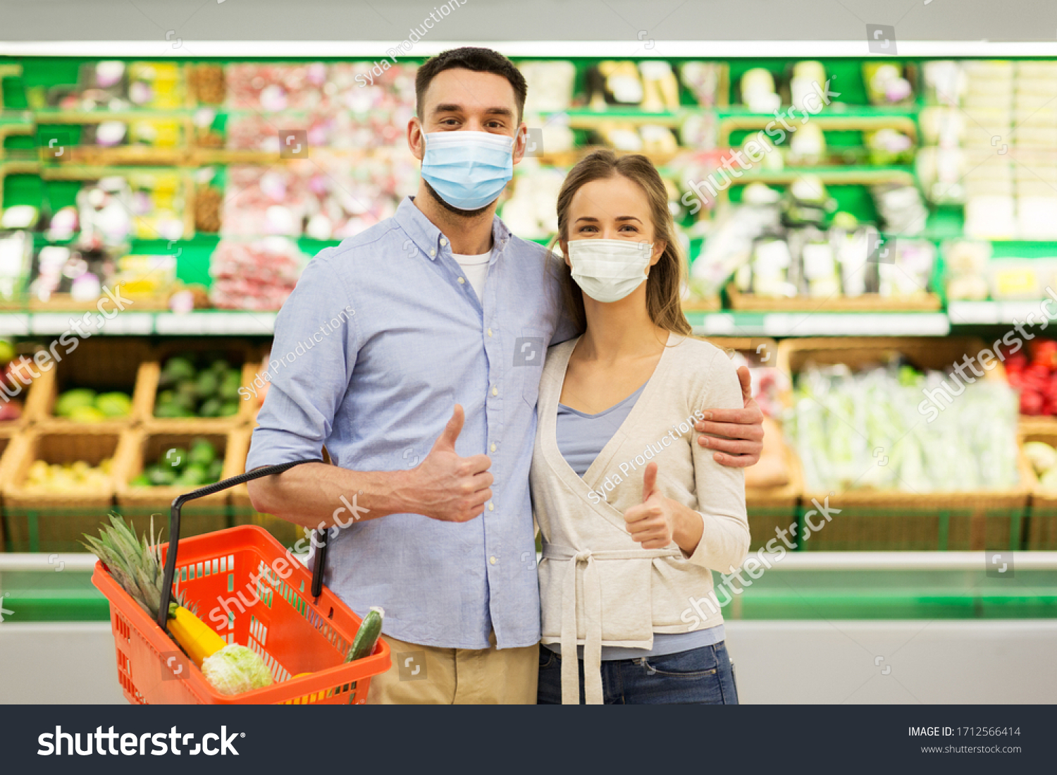 shopping, sale, consumerism and people concept - happy couple wearing face protective medical masks for protection from virus disease with food basket at grocery store or supermarket showing thumbs up #1712566414